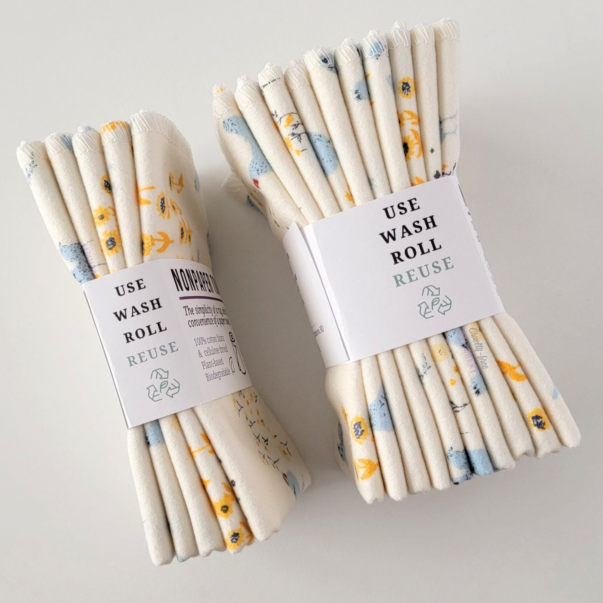 Two packages of the Hens and Sunflowers NonPaper Towels, shown on their side to display the 5-pack and 10-packs. The side of the paper tag says "use, wash, roll, reuse" and has the recycling logo with a leaf in the center, to symbolize they are biodegradable.