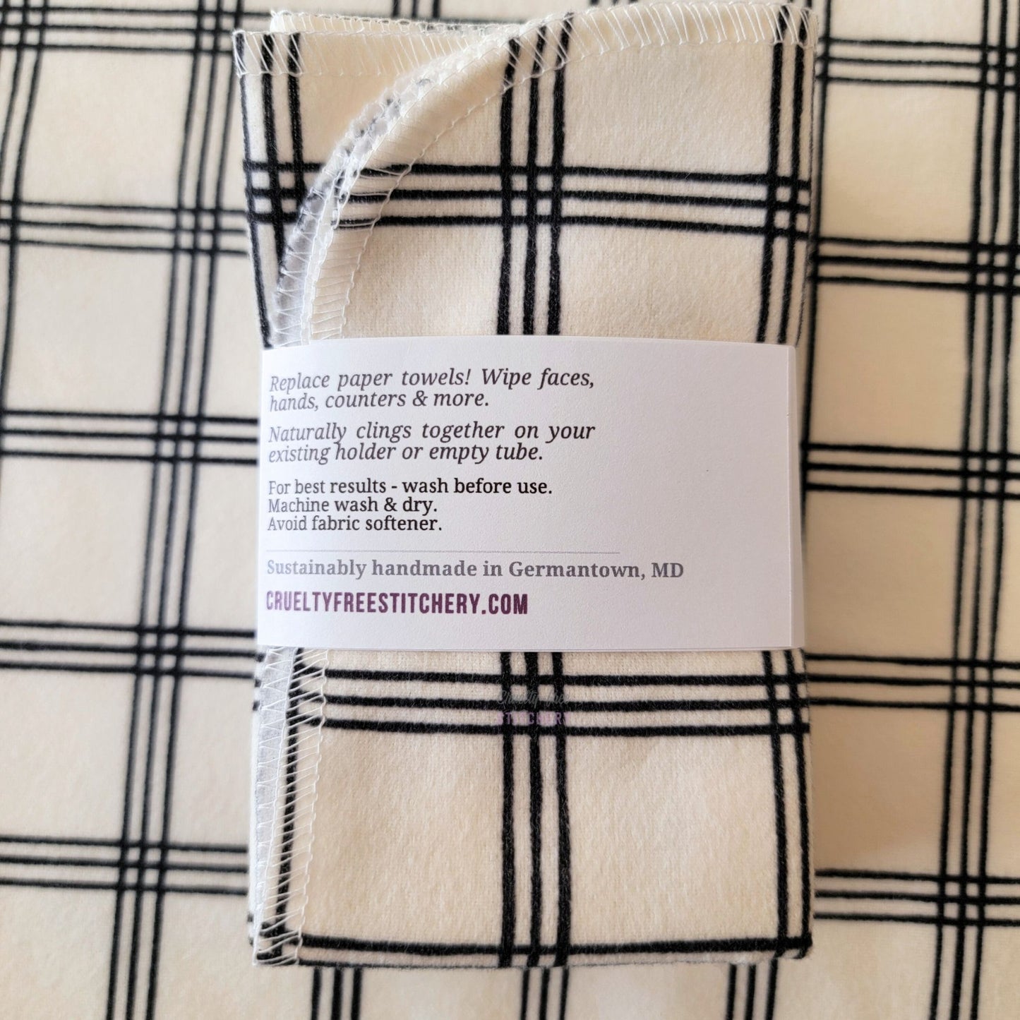 The back of a packaged bundle of the Ivory Black Crossroad NonPaper Towels. The tag reads "Replace paper towels! Wipe faces, hands, counters, and more. Naturally clings together on your existing holder or empty tube. For best results - wash before use. Machine wash and dry. Avoid fabric softener. Sustainable handmade in Germantown, Maryland. CrueltyFreeStitchery dot com."