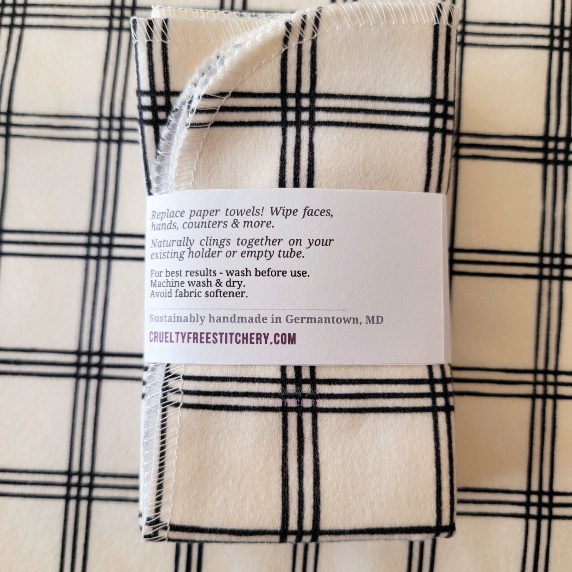 The back of a packaged bundle of the Ivory Black Crossroad NonPaper Towels. The tag reads "Replace paper towels! Wipe faces, hands, counters, and more. Naturally clings together on your existing holder or empty tube. For best results - wash before use. Machine wash and dry. Avoid fabric softener. Sustainable handmade in Germantown, Maryland. CrueltyFreeStitchery dot com."
