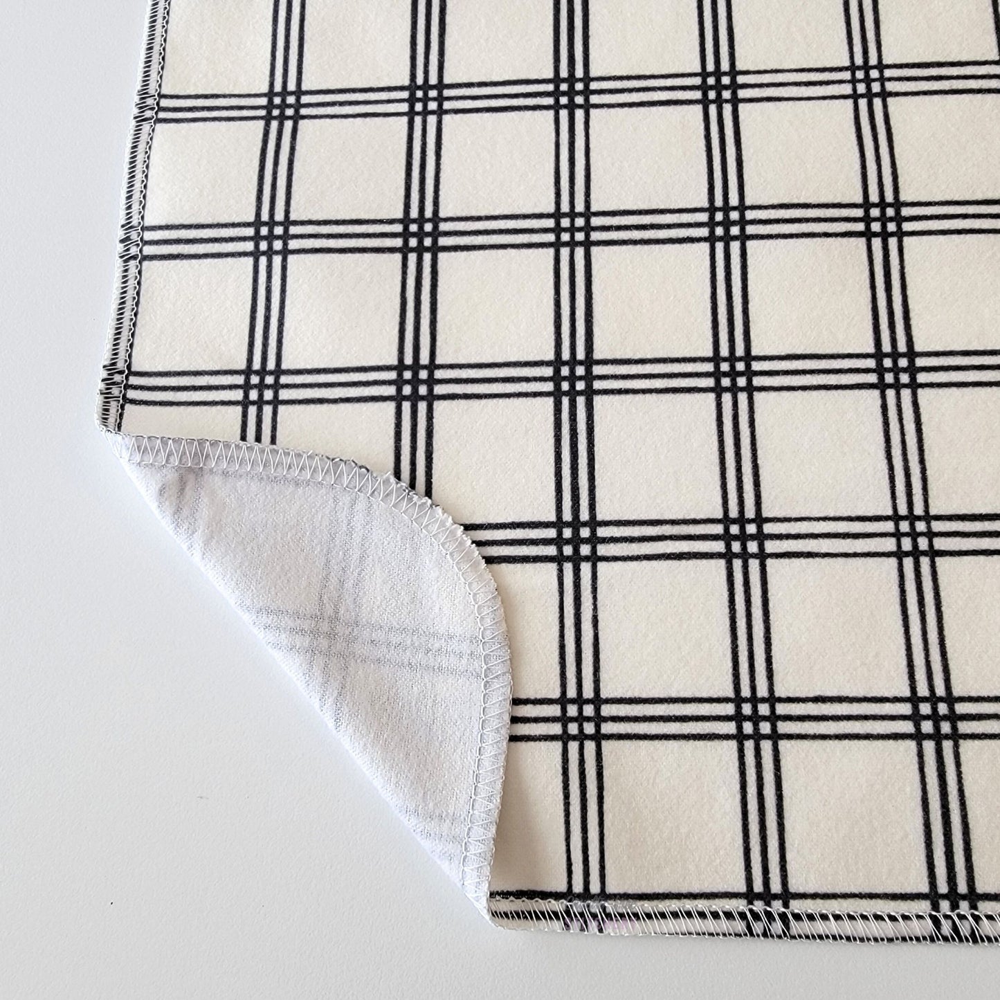 The Ivory Black Crossroad NonPaper Towel, shown close-up with the bottom corner folded back to show they are unprinted on the back side, and are one layer.