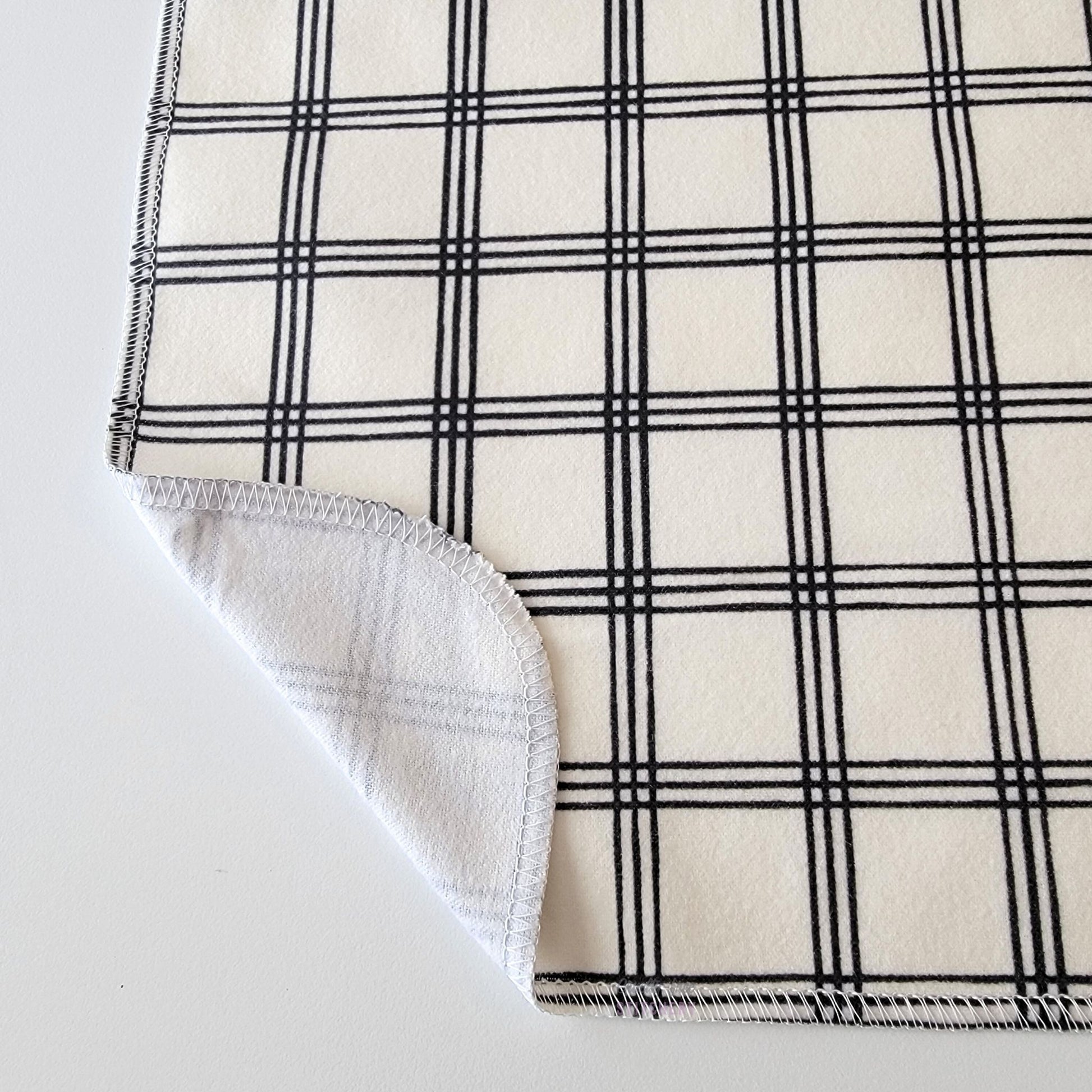 The Ivory Black Crossroad NonPaper Towel, shown close-up with the bottom corner folded back to show they are unprinted on the back side, and are one layer.