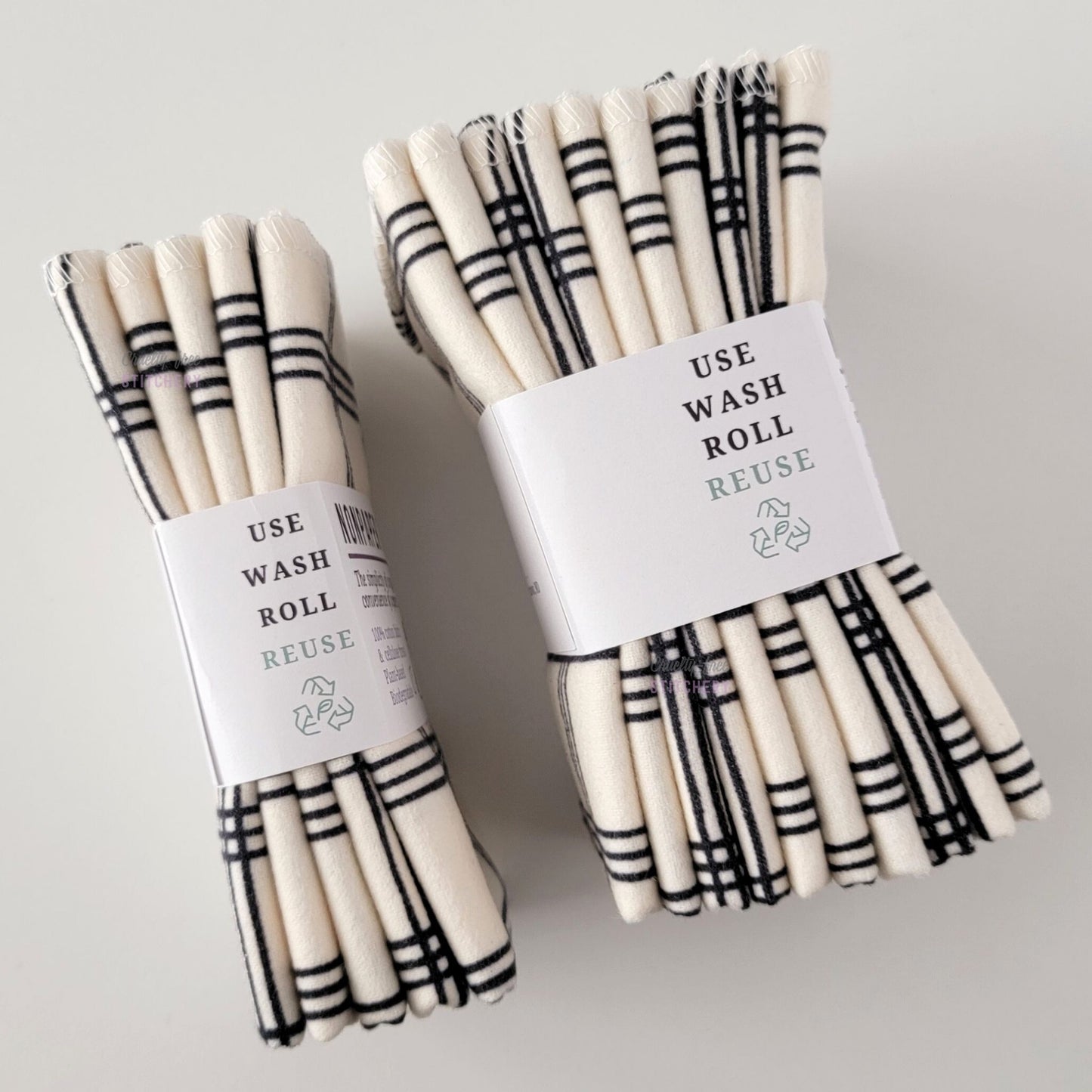 Two packages of the Ivory Black Crossroad NonPaper Towels, shown on their side to display the 5-pack and 10-packs. The side of the paper tag says "use, wash, roll, reuse" and has the recycling logo with a leaf in the center, to symbolize they are biodegradable.
