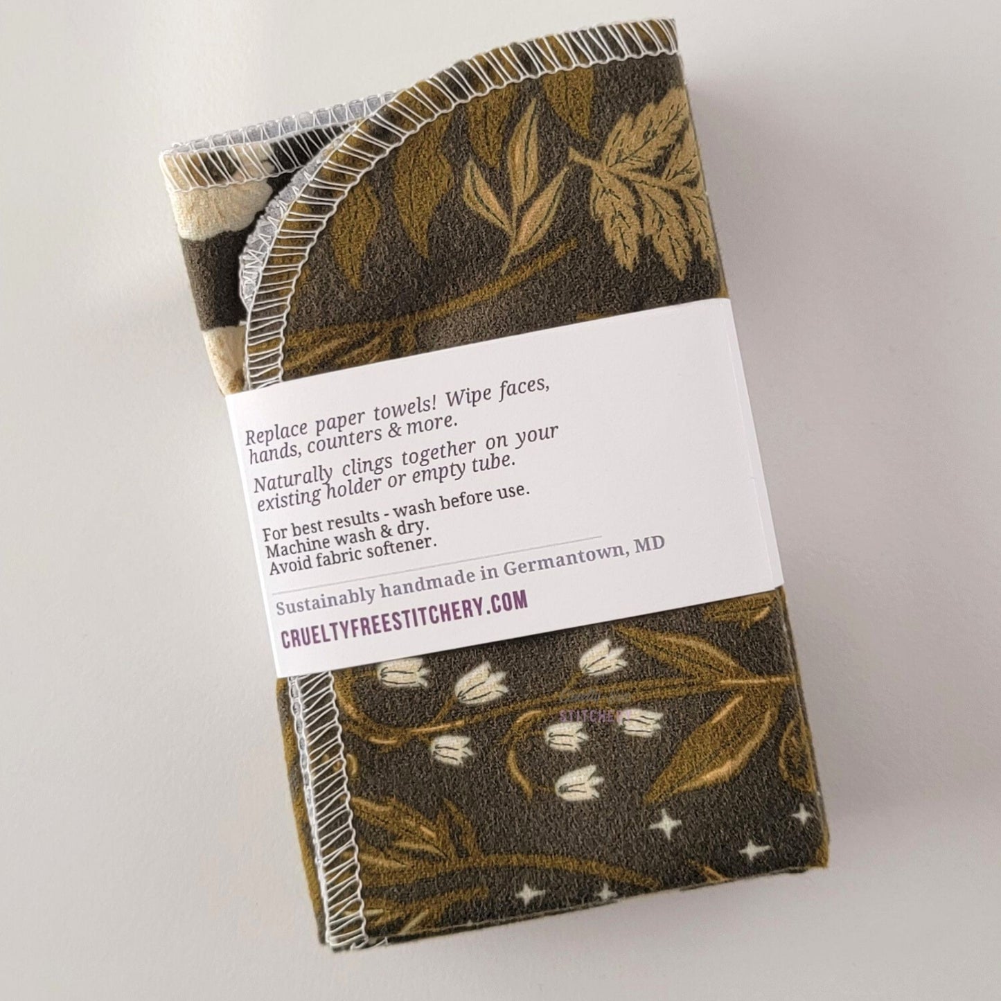 The back of a packaged bundle of the Lunar Forest NonPaper Towels. The tag reads "Replace paper towels! Wipe faces, hands, counters, and more. Naturally clings together on your existing holder or empty tube. For best results - wash before use. Machine wash and dry. Avoid fabric softener. Sustainable handmade in Germantown, Maryland. CrueltyFreeStitchery dot com."