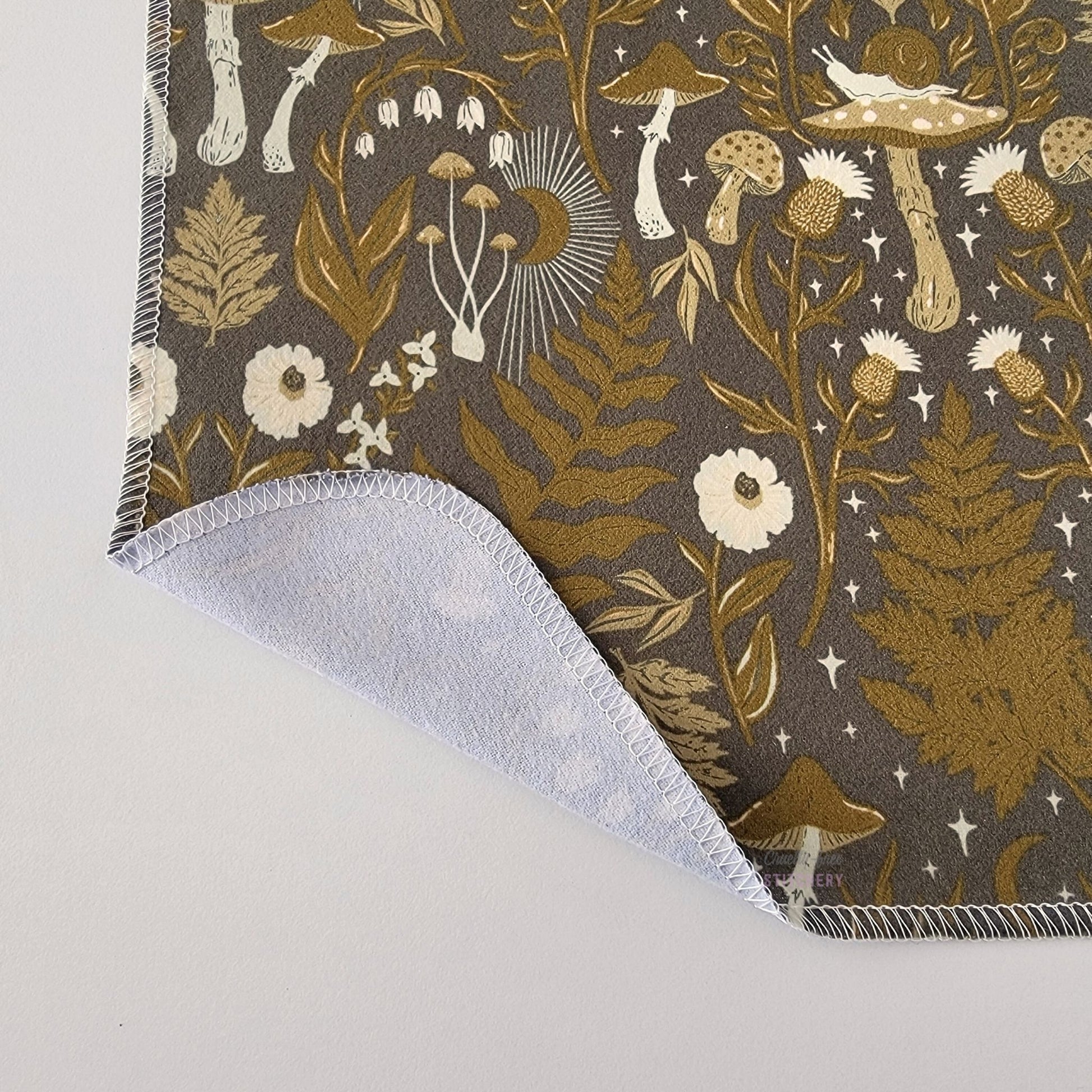 The Lunar Forest NonPaper Towel, shown close-up with the bottom corner folded back to show they are unprinted on the back side, and are one layer.