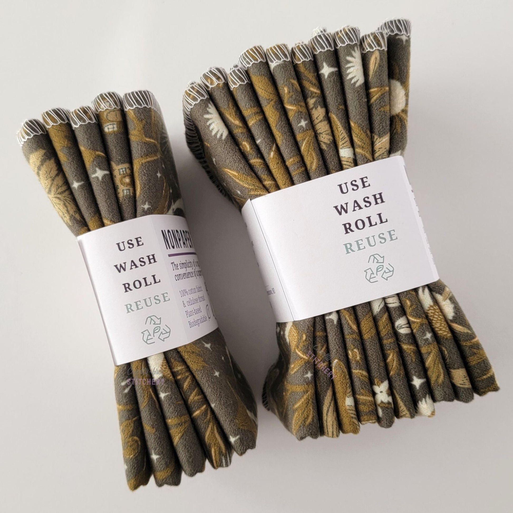 Two packages of the Lunar Forest NonPaper Towels, shown on their side to display the 5-pack and 10-packs. The side of the paper tag says "use, wash, roll, reuse" and has the recycling logo with a leaf in the center, to symbolize they are biodegradable.