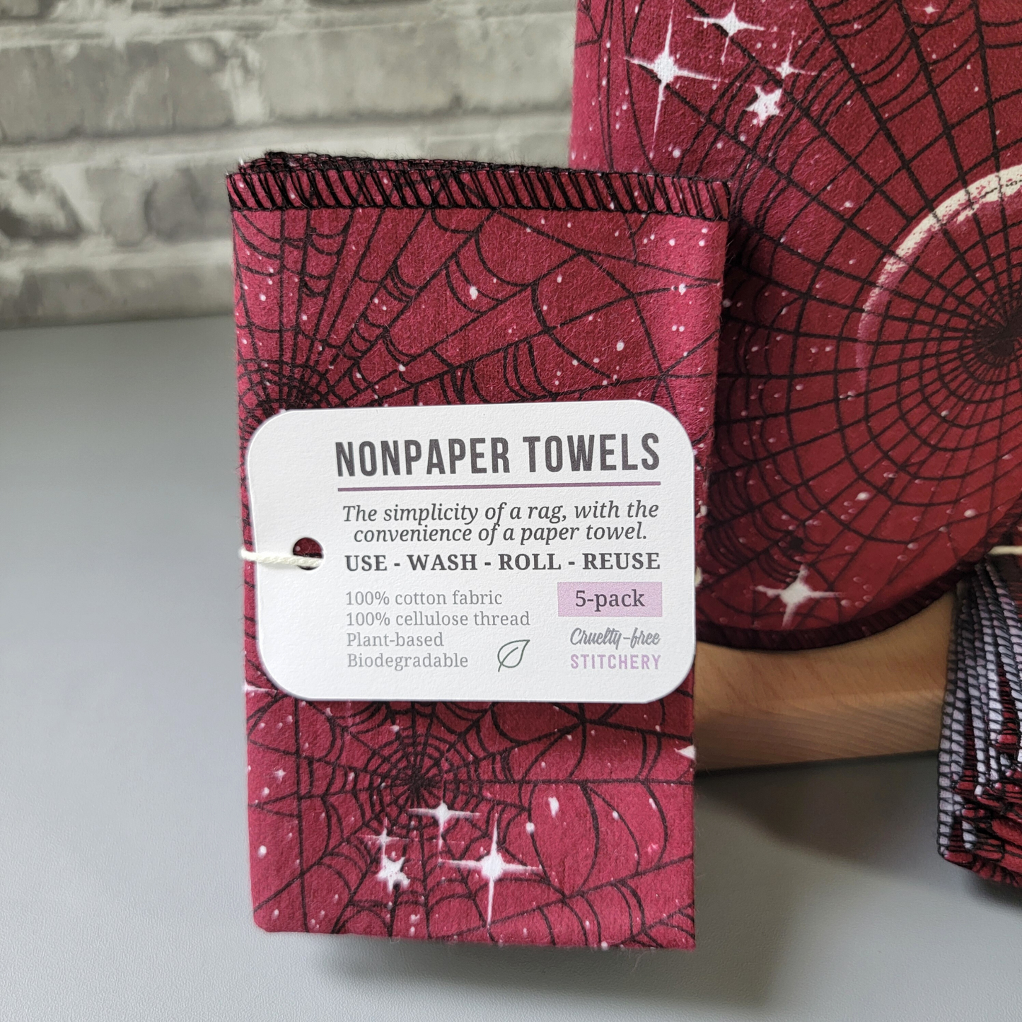 Close-up of a 5-pack of the Red Moon Web NonPaper Towels. The tag reads "nonpaper towels, the simplicity of a rag with the convenience of a paper towel. Use wash roll reuse. 100% cotton fabric, 100% cellulose thread, plant-based, biodegradable. 5-pack, cruelty-free stitchery" with a tiny leaf.