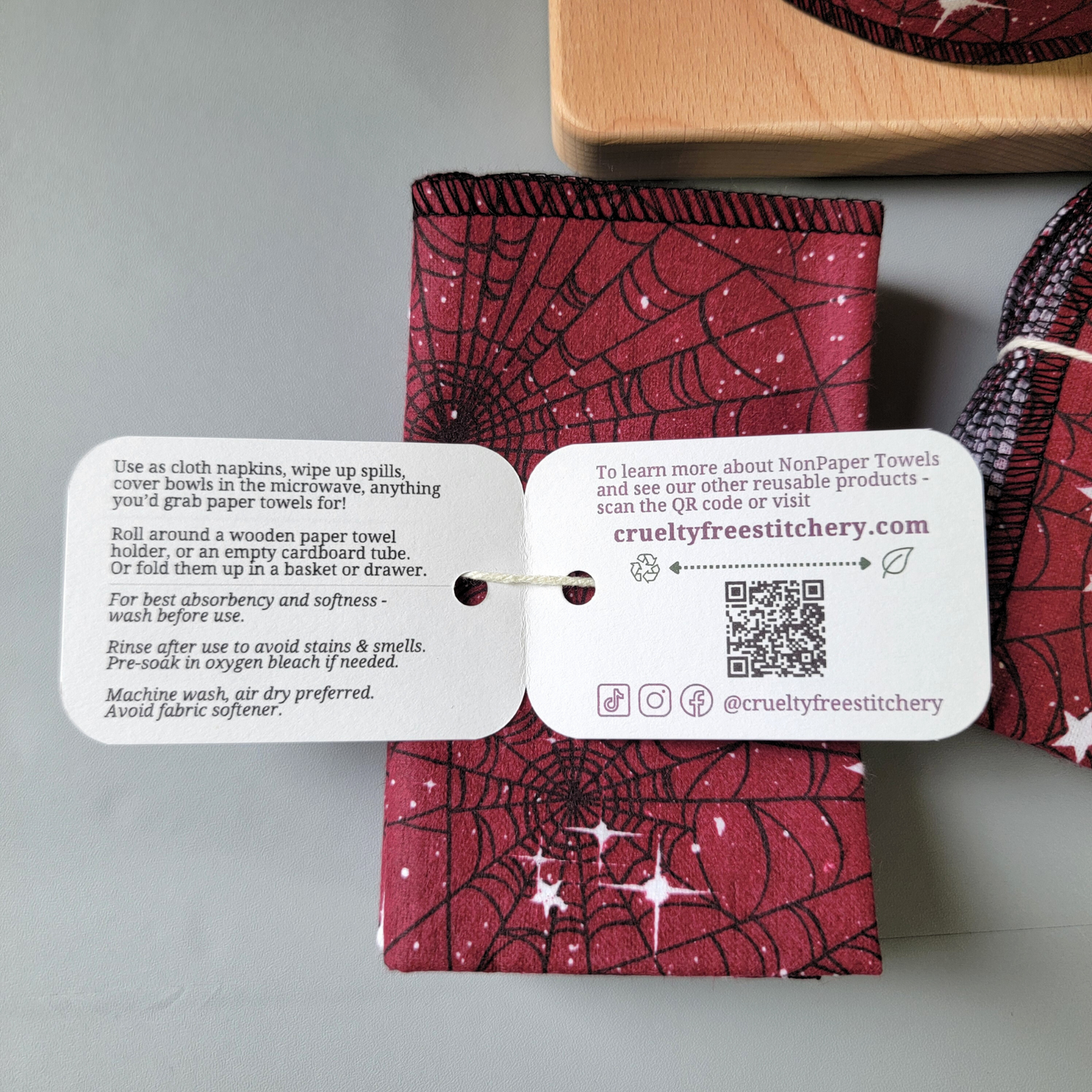 Inside the tag of the red moon web nonpaper towels, with care instructions and summary of description below. Other side has our website, a QR code, and social media handles @crueltyfreestitchery. 