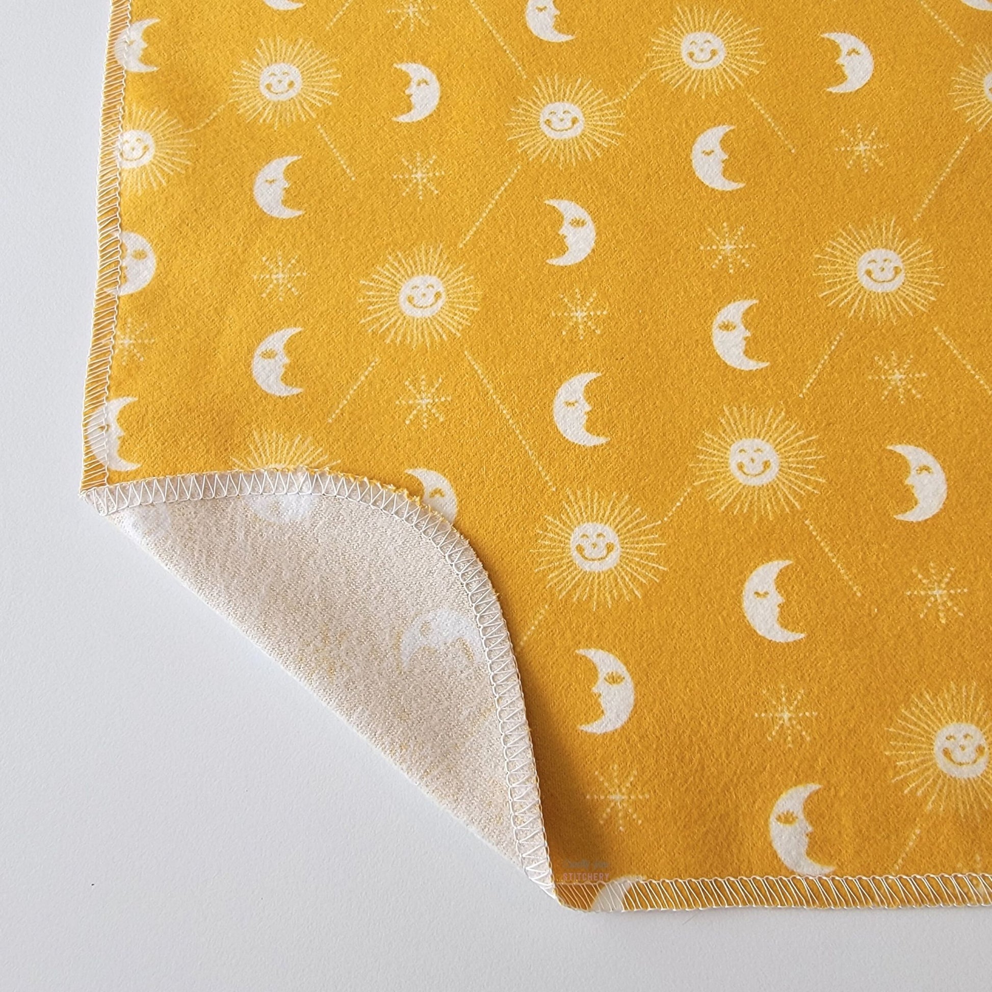 The mustard yellow celestial NonPaper Towel, shown close-up with the bottom corner folded back to show they are unprinted on the back side, and are one layer.