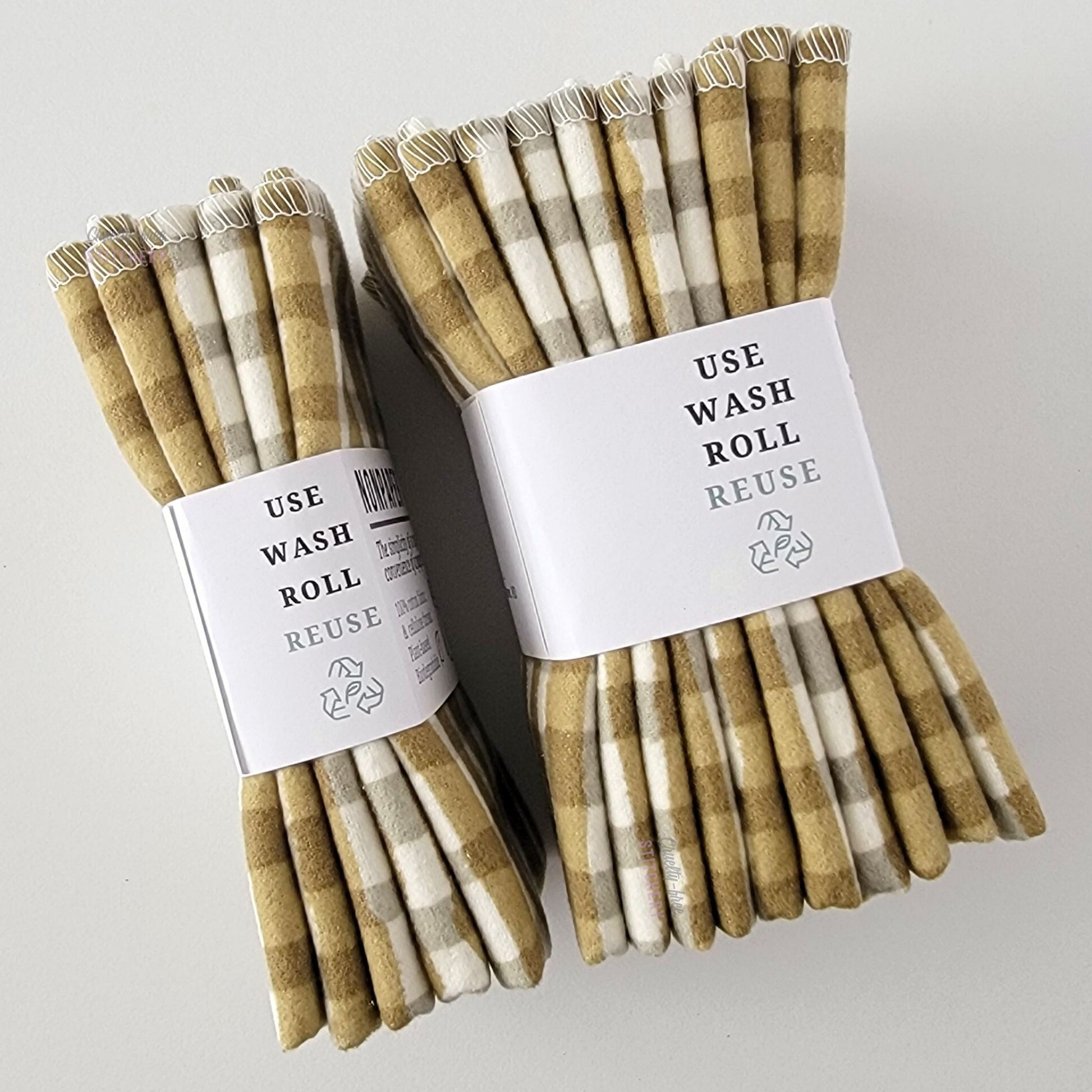 Two packages of the Olive Painted Plaid NonPaper Towels, shown on their side to display the 5-pack and 10-packs. The side of the paper tag says "use, wash, roll, reuse" and has the recycling logo with a leaf in the center, to symbolize they are biodegradable.