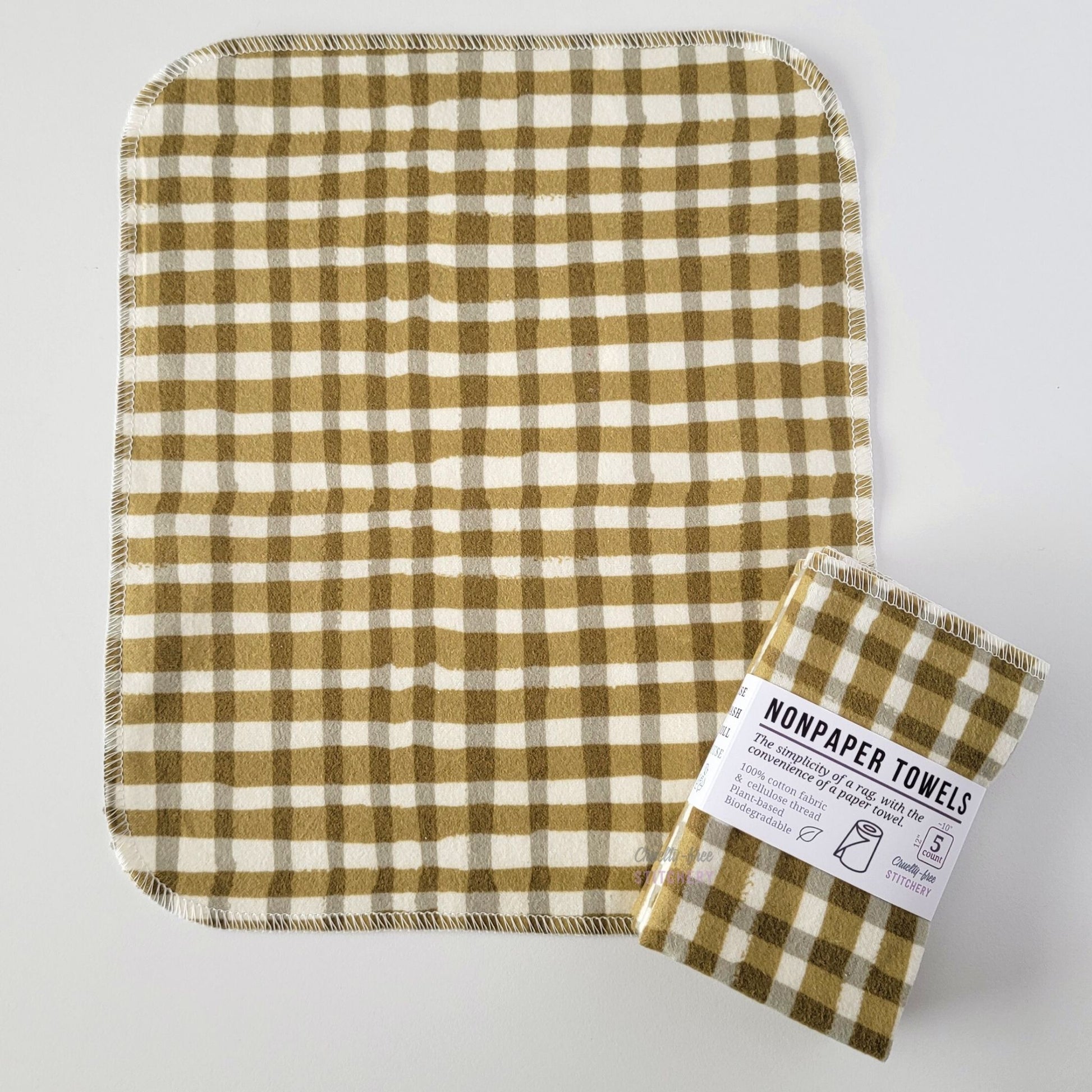 An unfolded Olive Painted Plaid NonPaper Towel, next to a bundled 5-pack. The towel is a rectangle with rounded corners, stitched around the edges with white thread. The bundled pack is folded up with a paper wrapper that says "NonPaper Towels, the simplicity of a rag with the convenience of a paper towel"