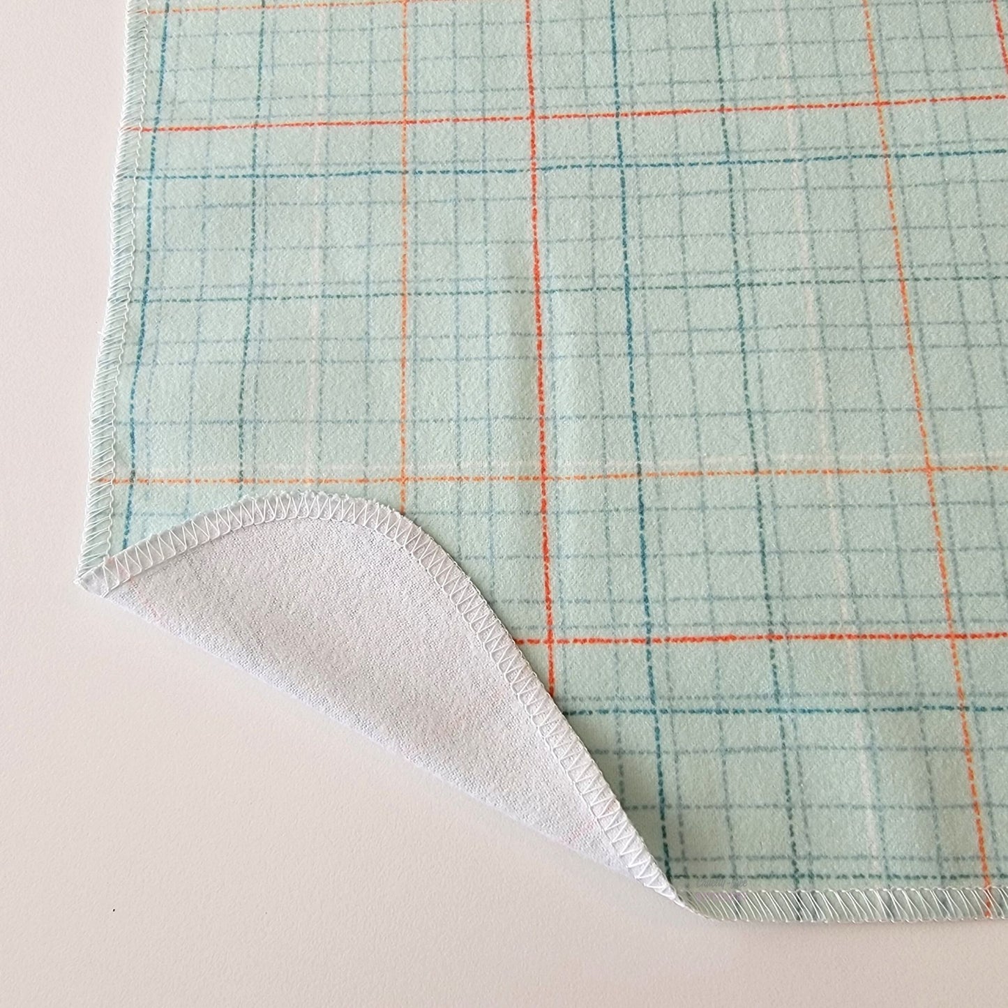 The Pale Blue Grid NonPaper Towel, shown close-up with the bottom corner folded back to show they are unprinted on the back side, and are one layer.