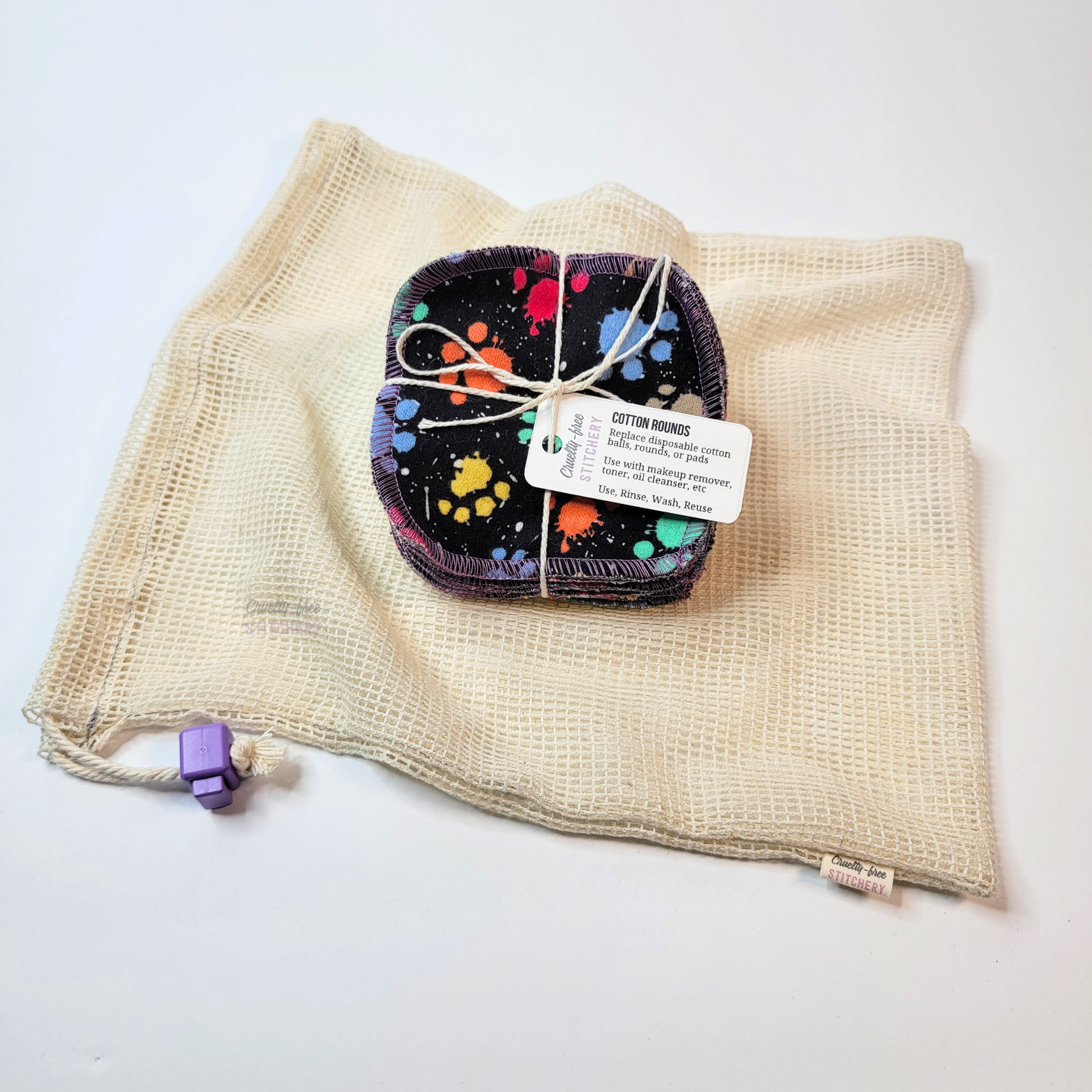 A bundled pack of cotton rounds on top of a cotton mesh washing bag. It has a drawstring and a purple square cord stopper.
