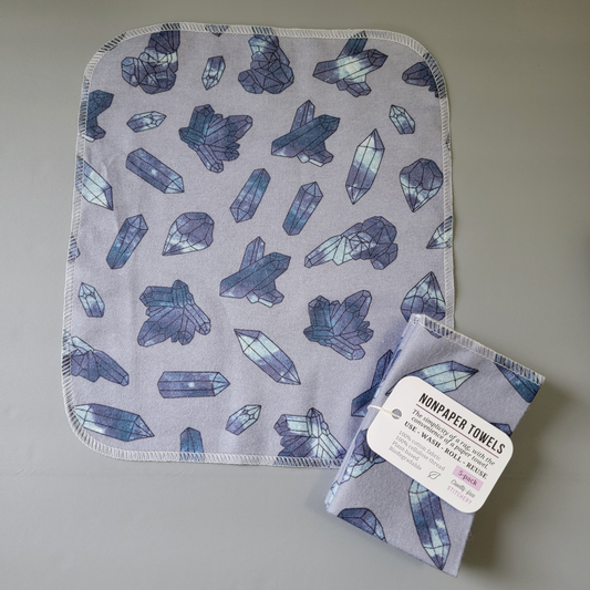 The purple crystals nonpaper towel laid flat to show the print and shape. They are a rounded rectangle, and stitched around the edges with off-white thread. Some crystals are less than an inch long, others are in clusters that are about 2 inches wide. 