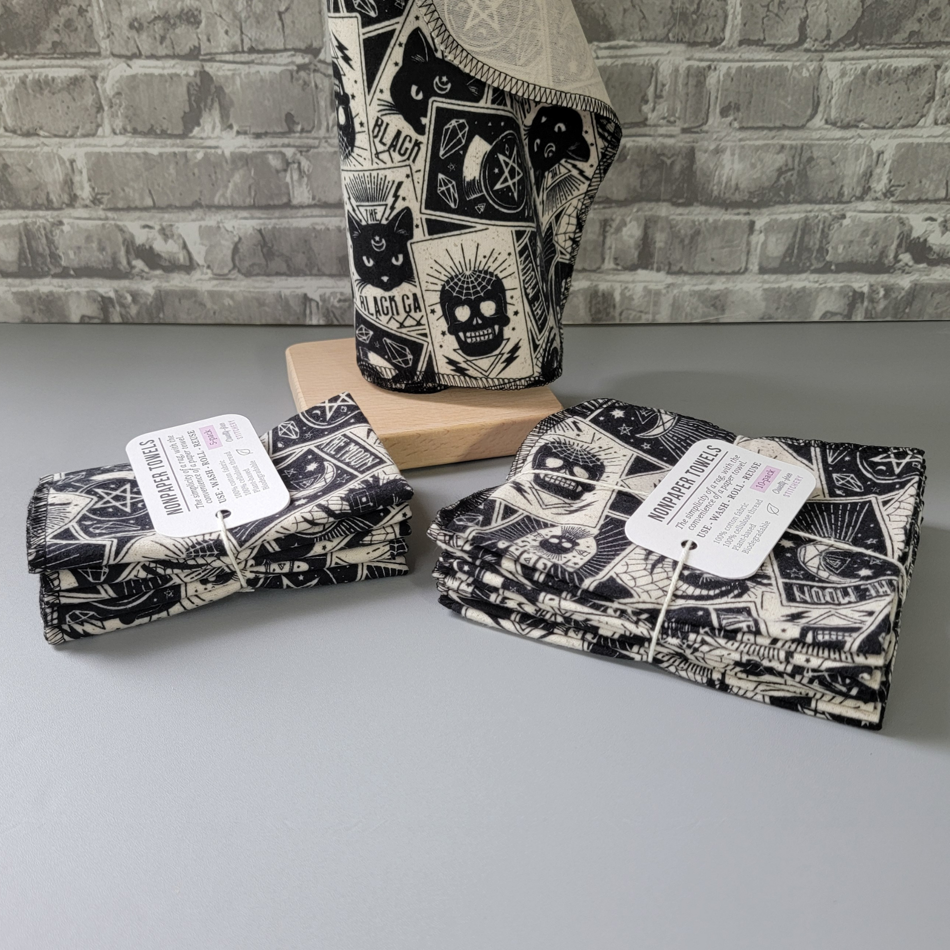 A 5-pack and 10-pack next to each other, photographed from the side to show the difference. The 10-pack has the towels folded in half twice, while the 5-pack has them folded one more time, making them look smaller. Both are tied with a cotton string and a small white paper tag.