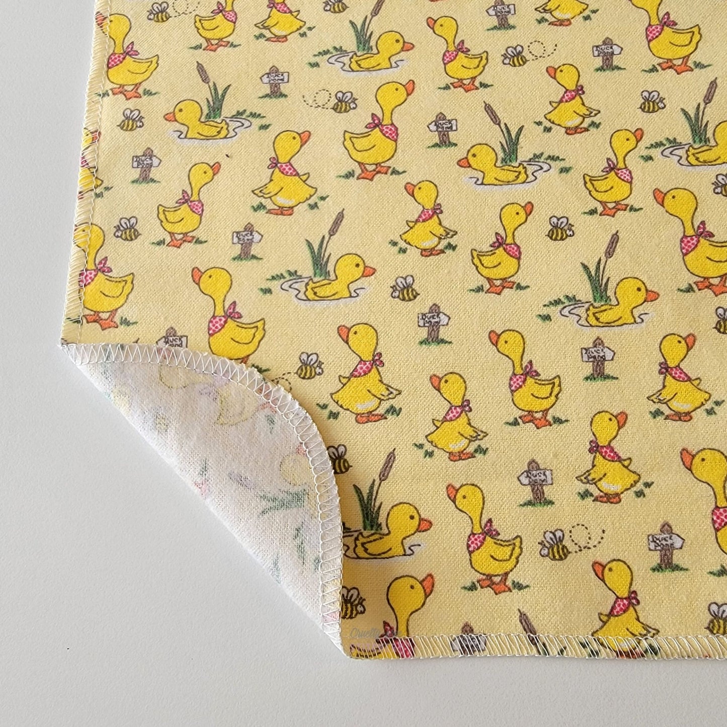 The Yellow Ducklings NonPaper Towel, shown close-up with the bottom corner folded back to show they are unprinted on the back side, and are one layer.
