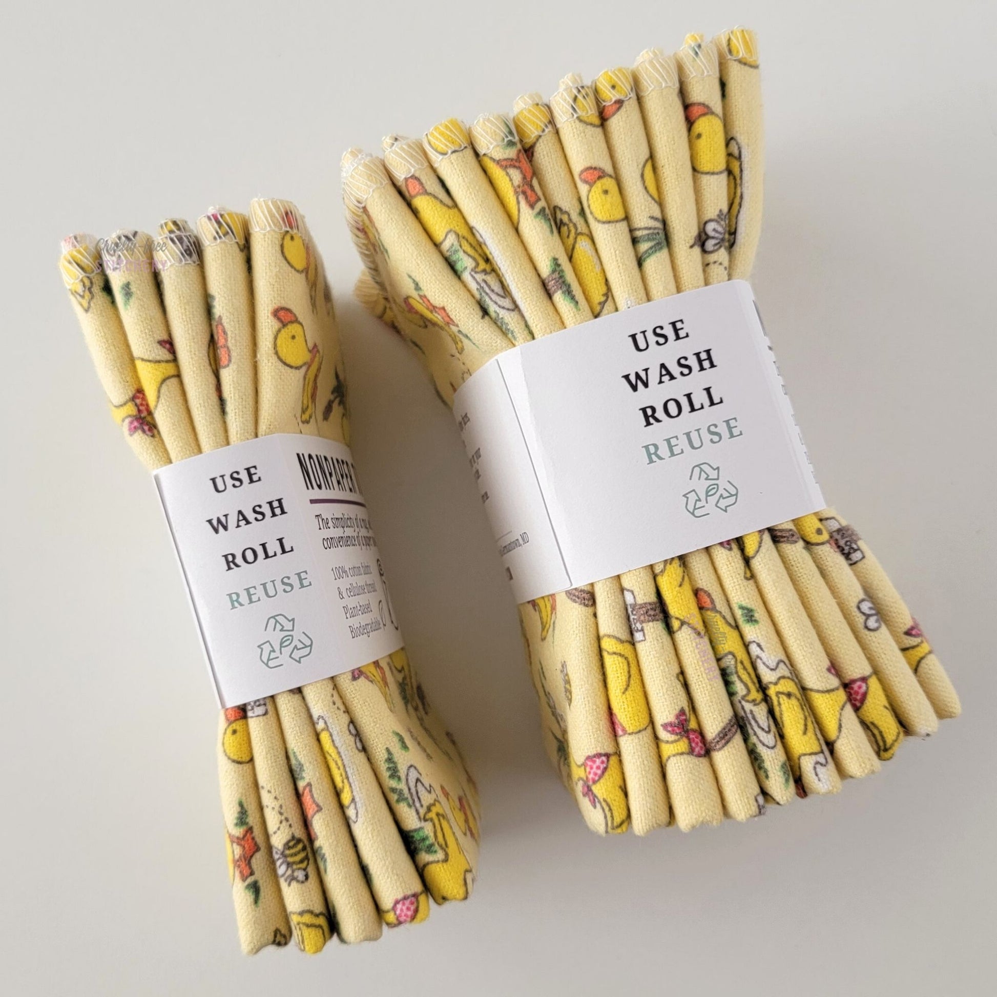Two packages of the Yellow Ducklings NonPaper Towels, shown on their side so display the 5-pack and 10-packs. The side of the paper tag says "use, wash, roll, reuse" and has the recycling logo with a leaf in the center, to symbolize they are biodegradable.