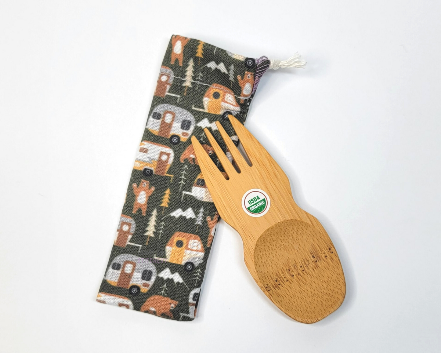 Reusable bamboo spork with pouch. The pouch is a dark green with vintage style campers, trees, and bears. The pouch is sitting diagonally with the spork partially on top pointing the other way. The spork is small, a double ended fork and spoon.