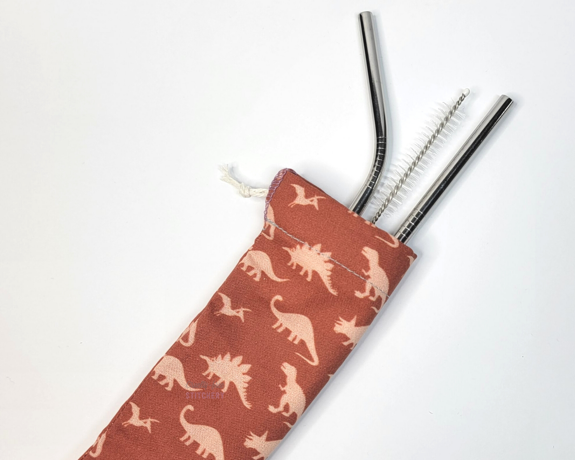 Reusable straw pouch with stainless steel straws sticking out the top. The fabric of the pouch is dark orange with light orange dinosaurs and it has a drawstring closure.