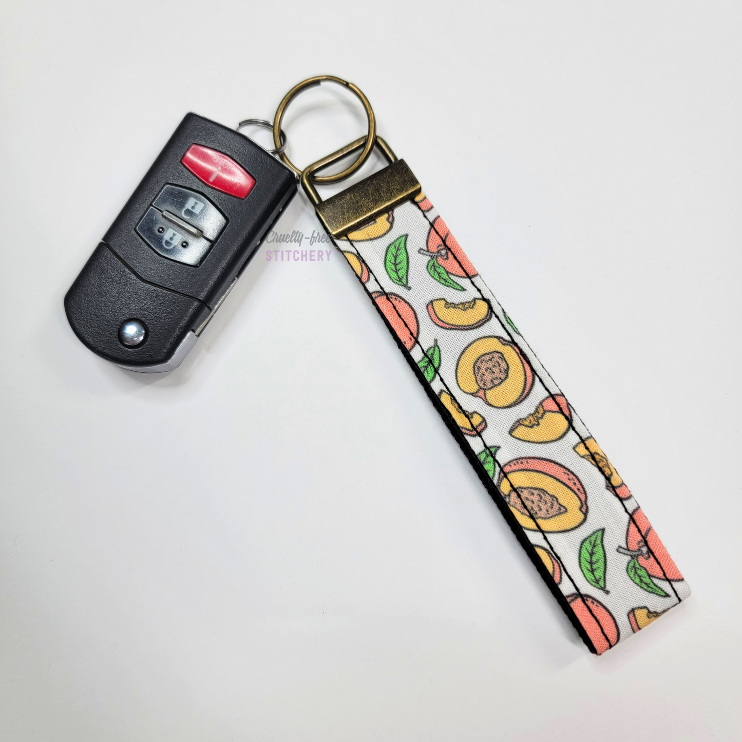 Peaches print key fob wristlet attached to a car key for scale. The car key is the fold-away type and is about half as long as the strap.