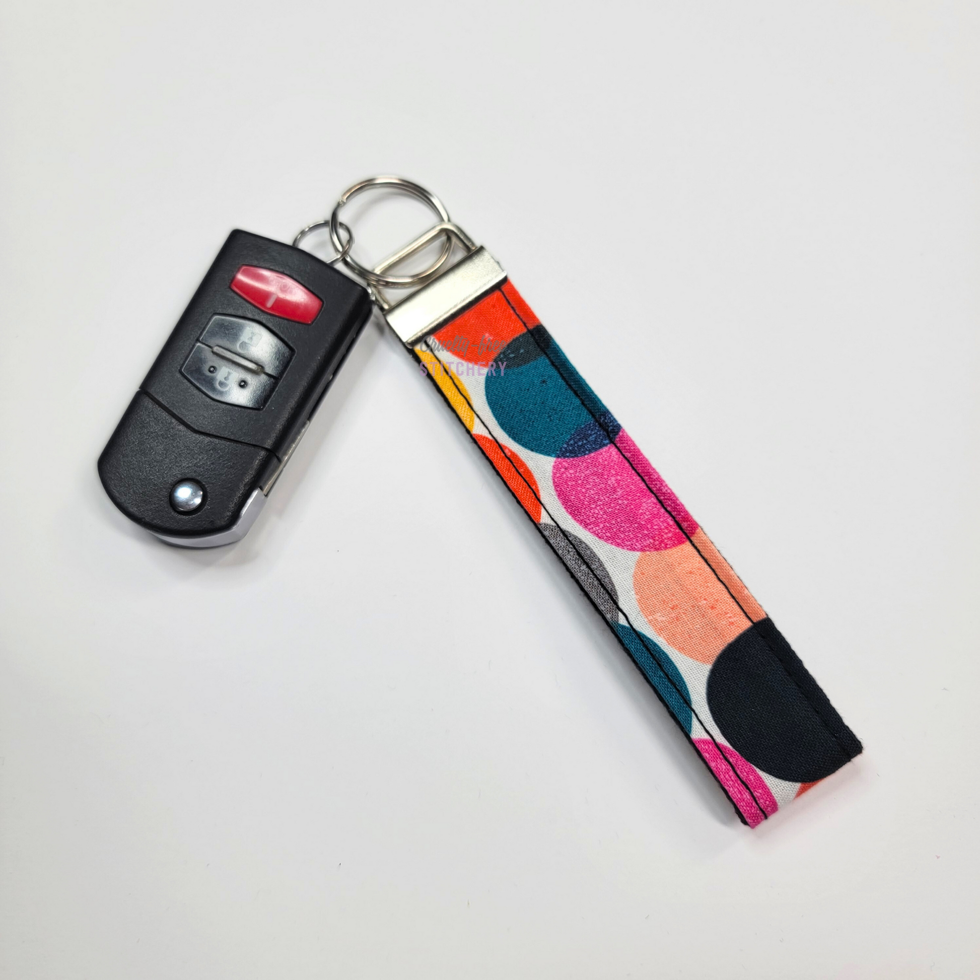Retro dots print key fob wristlet attached to a car key for scale. The car key is the fold-away type and is about half as long as the strap.