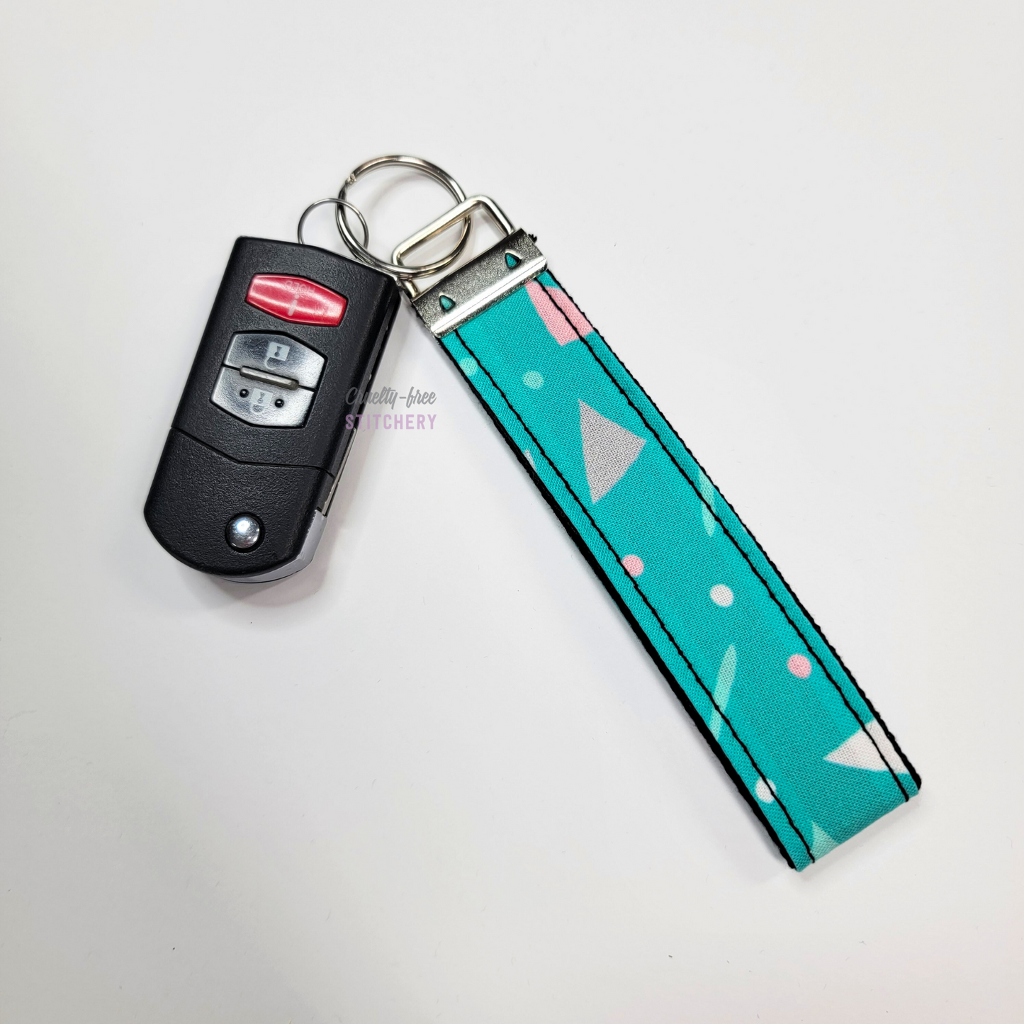90s print key fob wristlet attached to a car key for scale. The car key is the fold-away type and is about half as long as the strap.