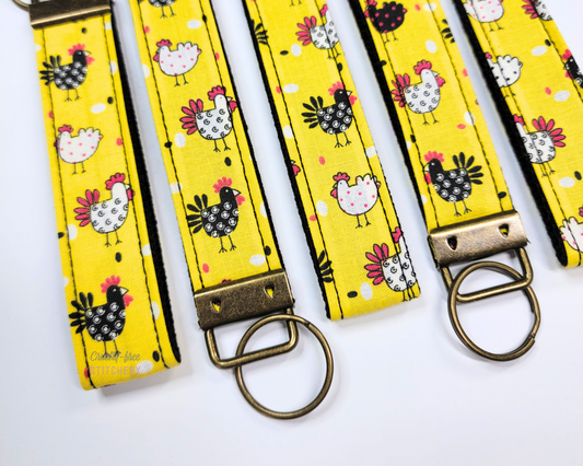 Yellow with chickens print wristlet keychains with brass hardware. The fabric is yellow with black and white tiny chickens.