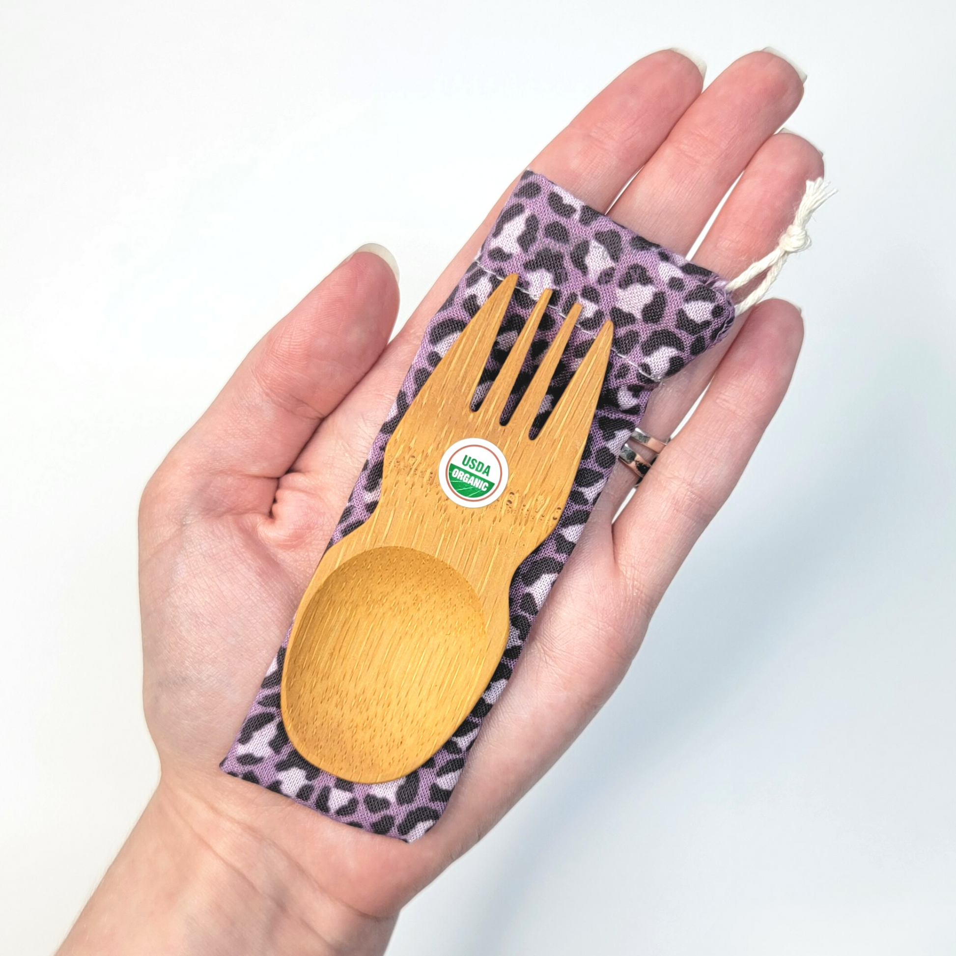 Violet leopard print fabric pouch with bamboo spork on top, laid on a hand for size reference. The spork is slightly longer than the fingers.