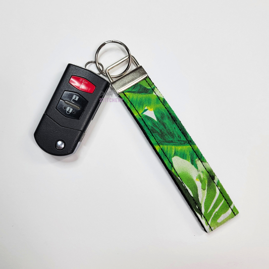 Camo print key fob wristlet attached to a car key for scale. The car key is the fold-away type and is about half as long as the strap.