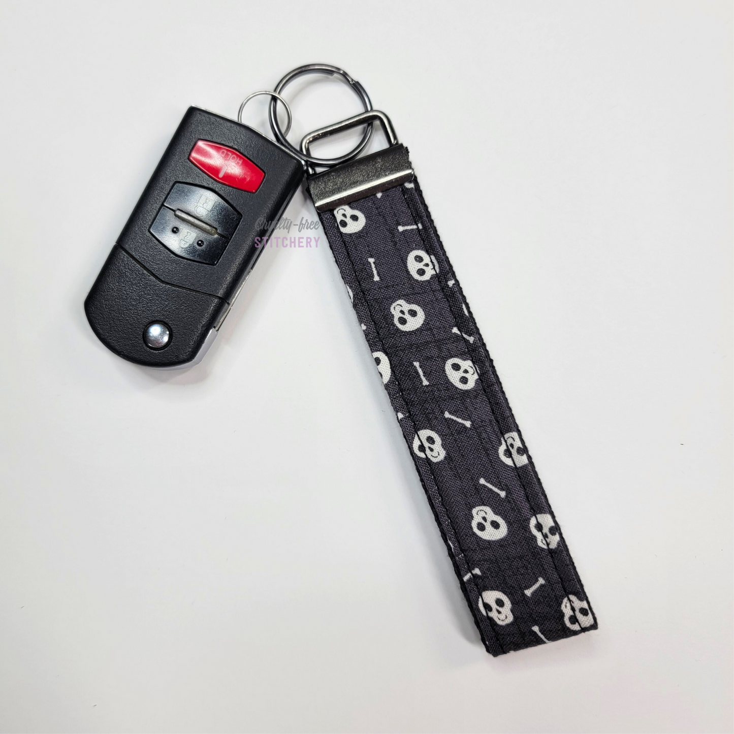 Skull print key fob wristlet attached to a car key for scale. The car key is the fold-away type and is about half as long as the strap.