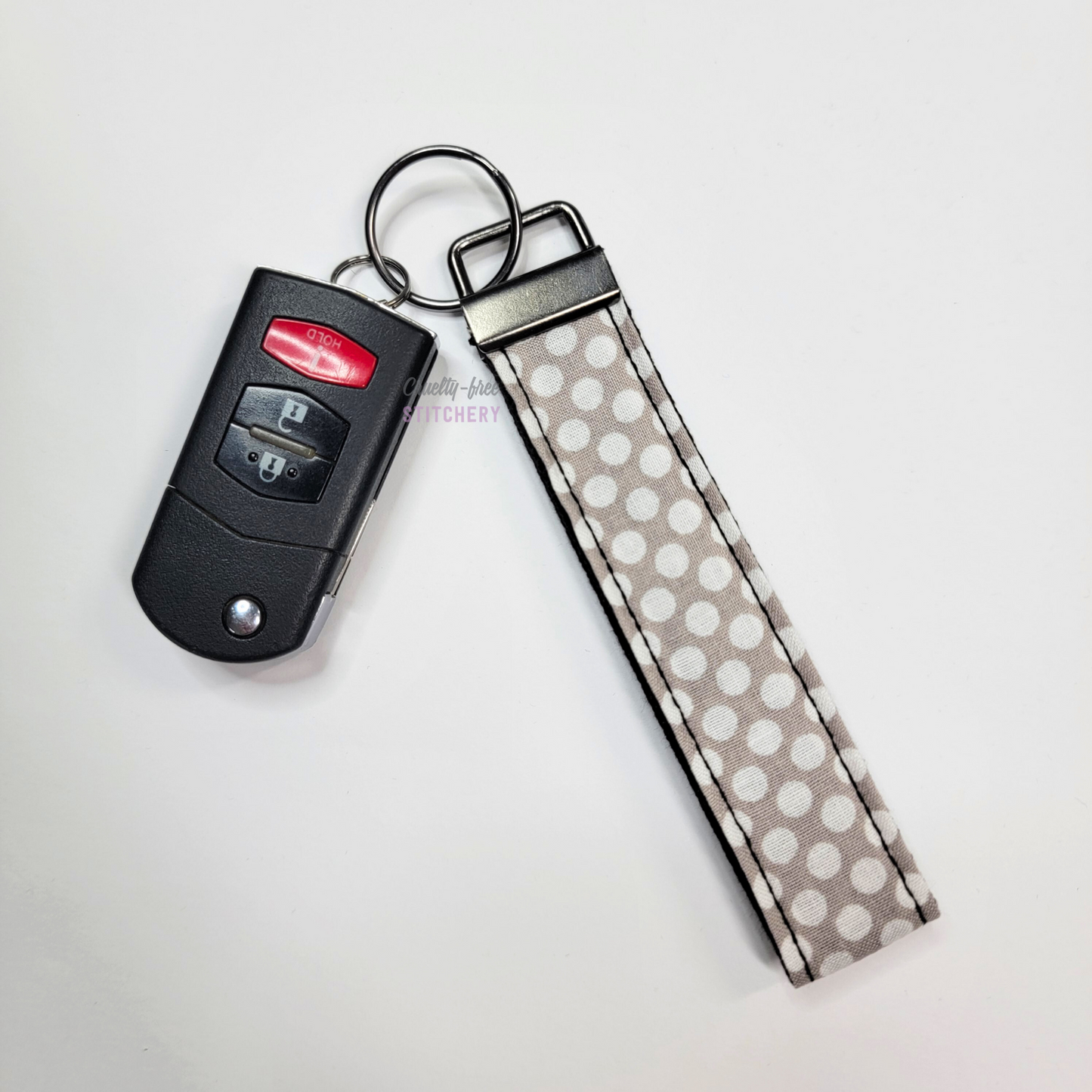 Grey and white dots print key fob wristlet attached to a car key for scale. The car key is the fold-away type and is about half as long as the strap.
