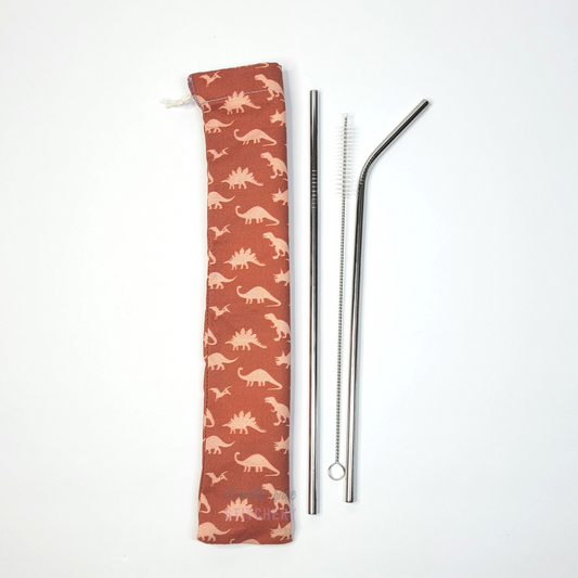 Reusable straw pouch in the same dinosaur print laying vertically next to a straw cleaner brush, a straight stainless steel straw, and a bent stainless steel straw.