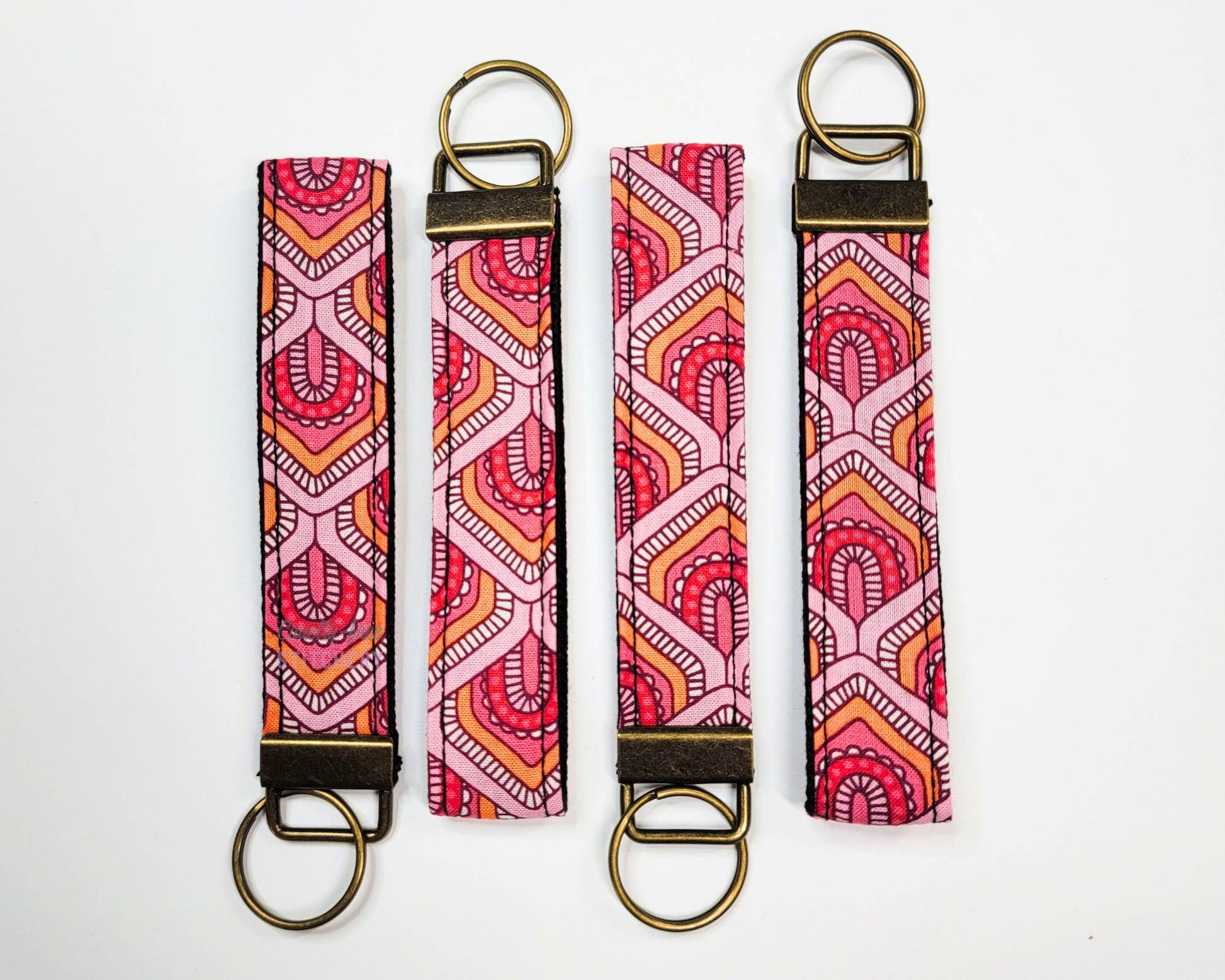 Four key fobs lined up in alternating directions. The wristlet straps are various shades of pink and orange with a large scaled pattern.