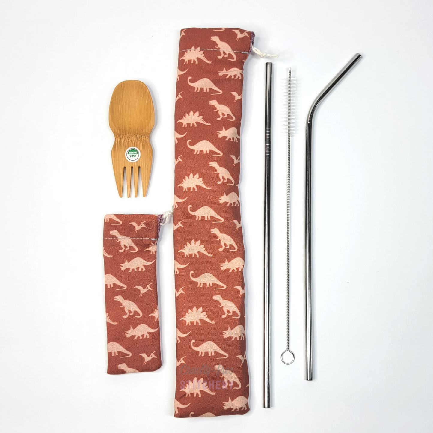 All contents of this bundle, a bamboo spork, dinosaur print spork pouch, dinosaur print straw pouch, and stainless steel straw set.