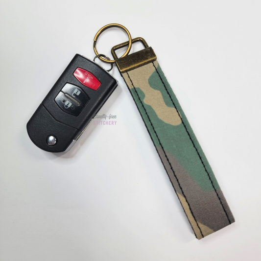 Camo print key fob wristlet attached to a car key for scale. The car key is the fold-away type and is about half as long as the strap.