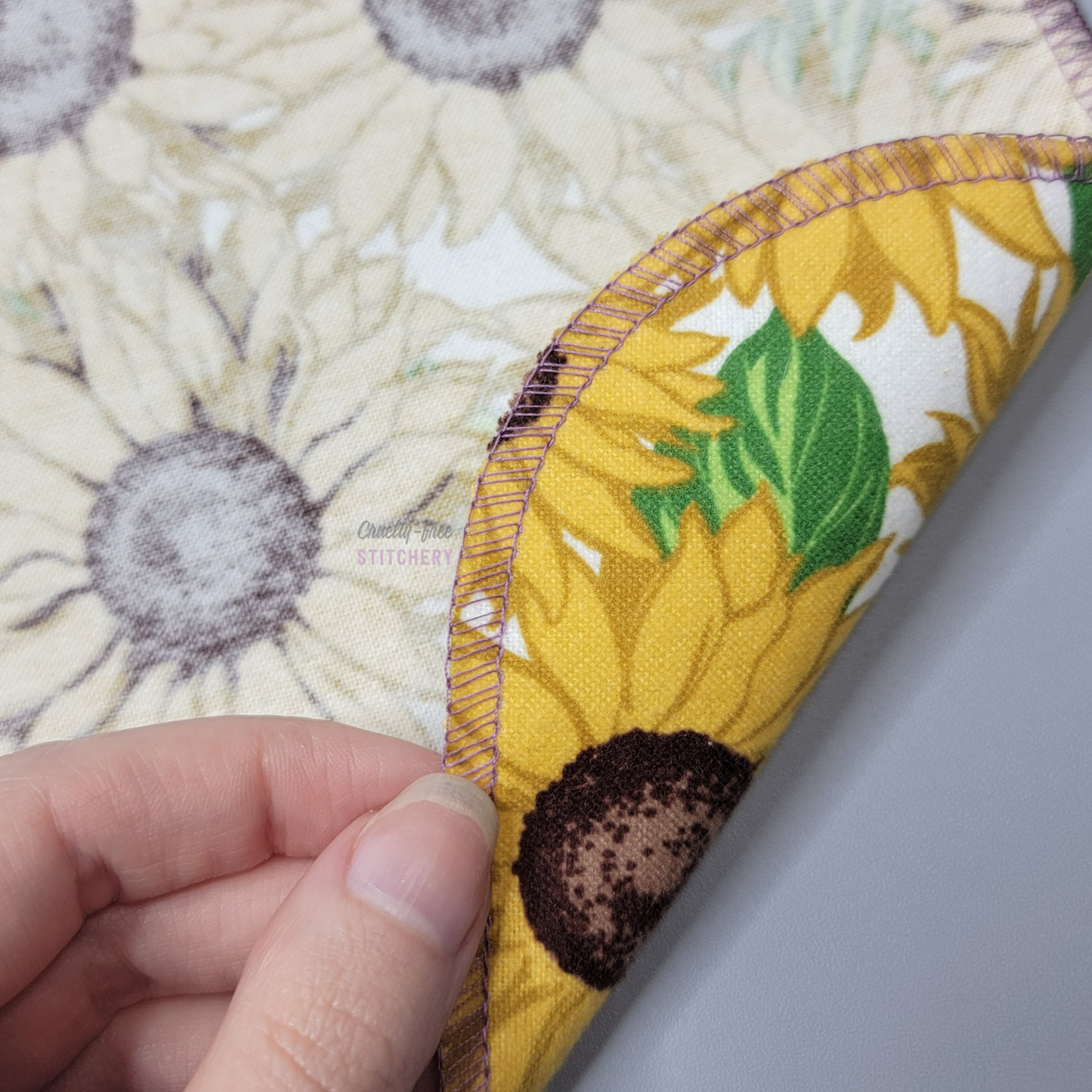 Lifting a corner of the sunflower NonPaper Towel to show the front, back, and a close-up of the stitching.