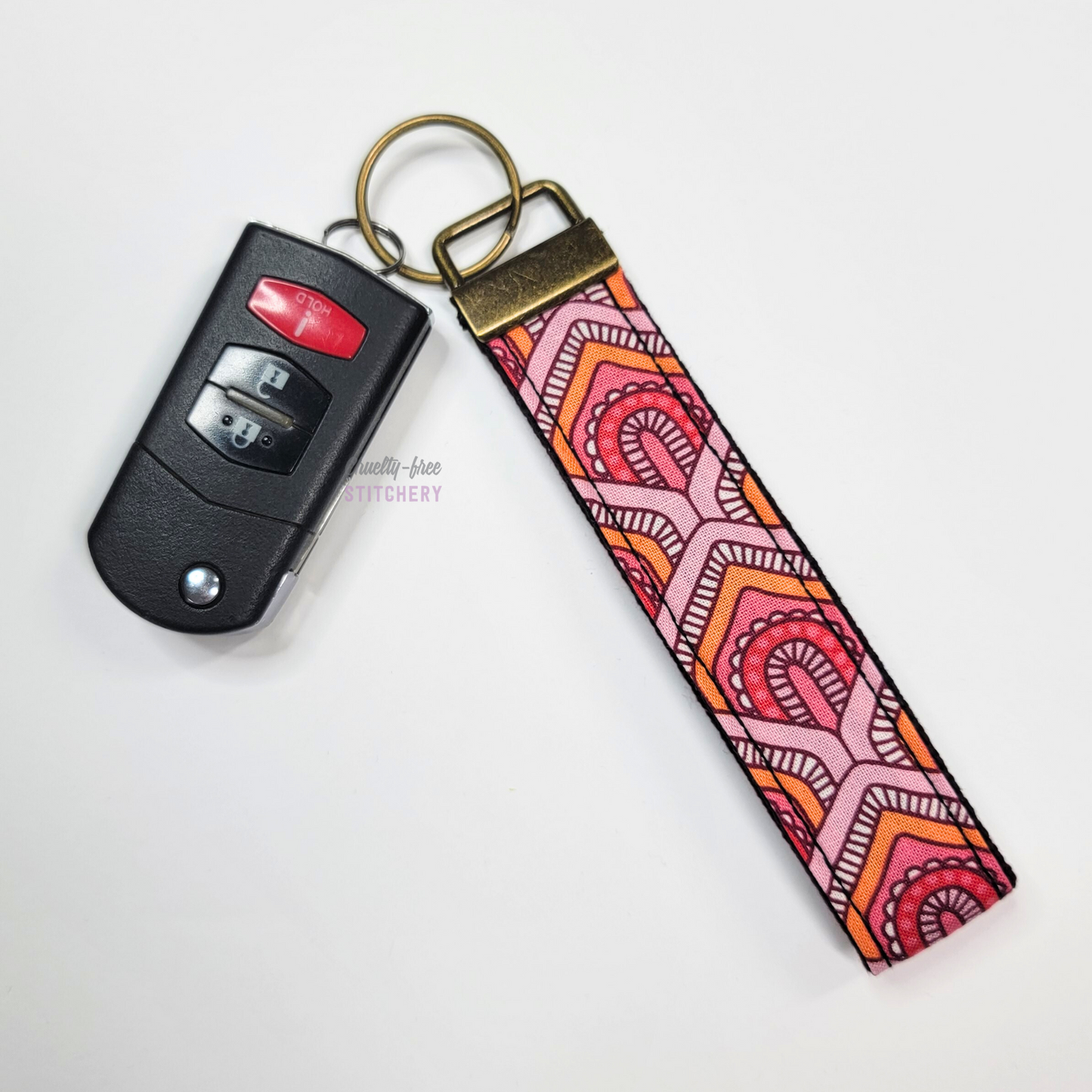 Pink and orange scales print key fob wristlet attached to a car key for scale. The car key is the fold-away type and is about half as long as the strap.