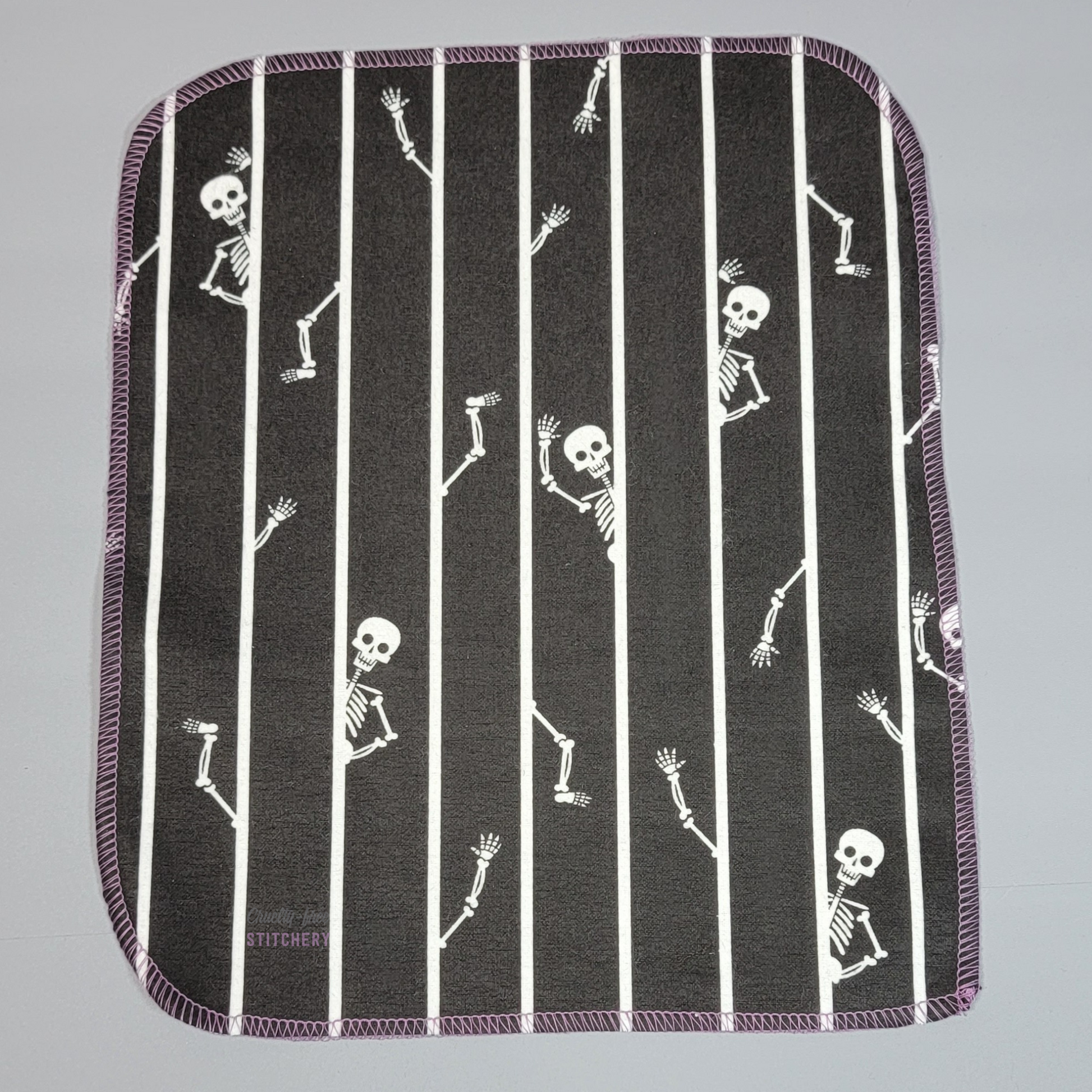 A black NonPaper Towel with vertical white stripes and skeleton heads, arms, and legs peeking out from behind the lines.