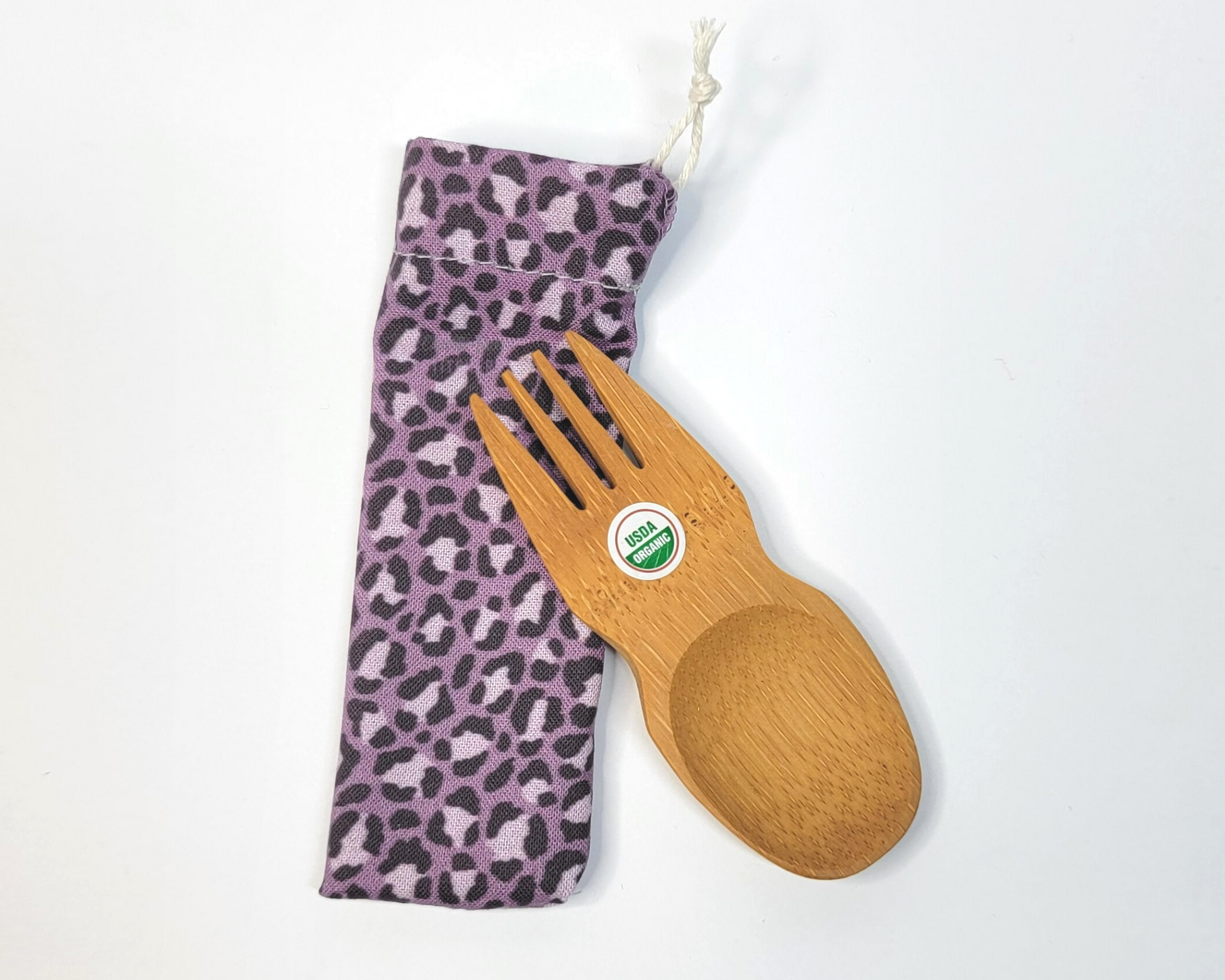 Reusable bamboo spork with pouch. The pouch is a muted violet leopard print. The pouch is sitting diagonally with the spork partially on top pointing the other way. The spork is small, a double ended fork and spoon.