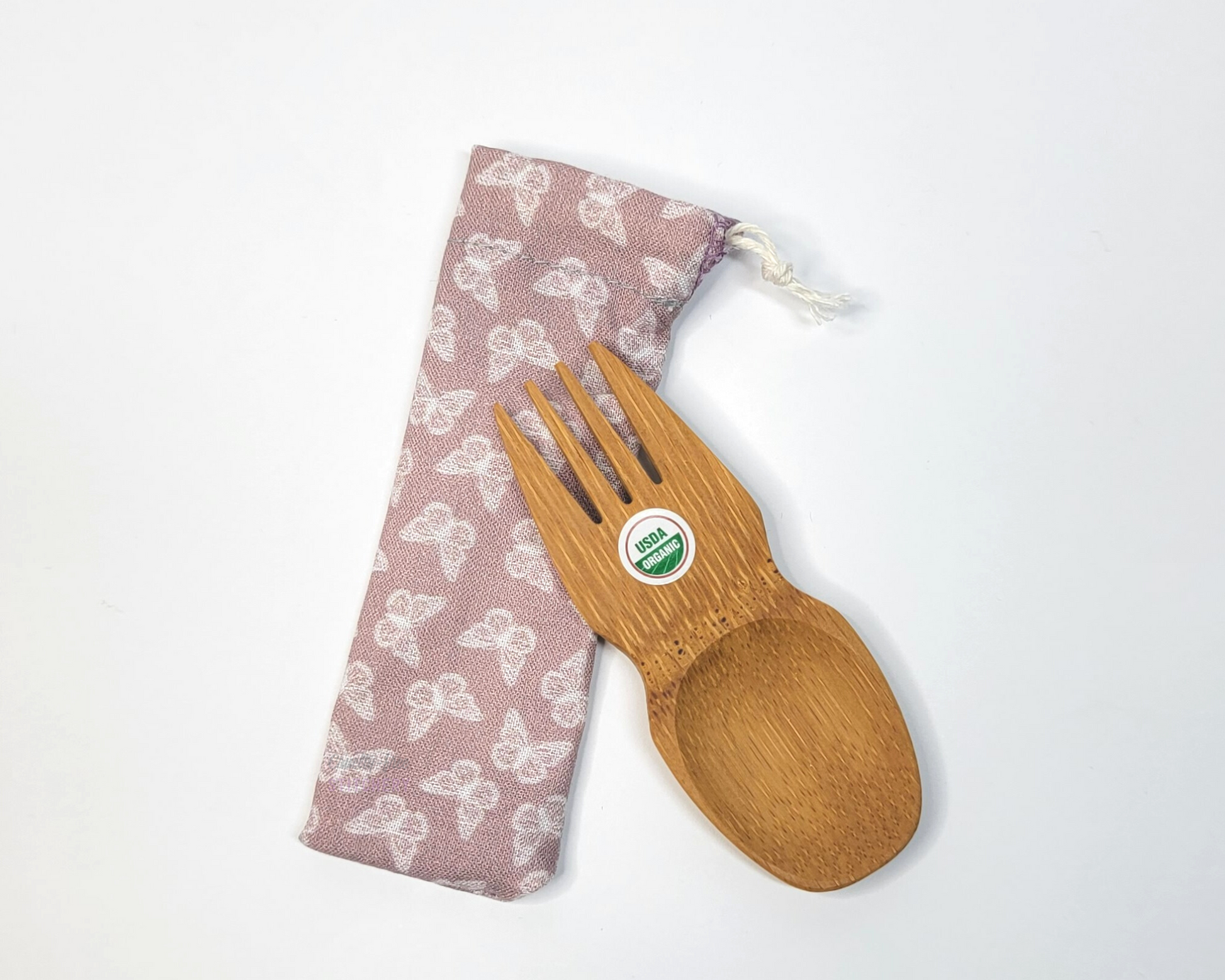 Reusable bamboo spork with pouch. The pouch is a light mauve pink with tiny white butterflies. The pouch is sitting diagonally with the spork partially on top pointing the other way. The spork is small, a double ended fork and spoon.
