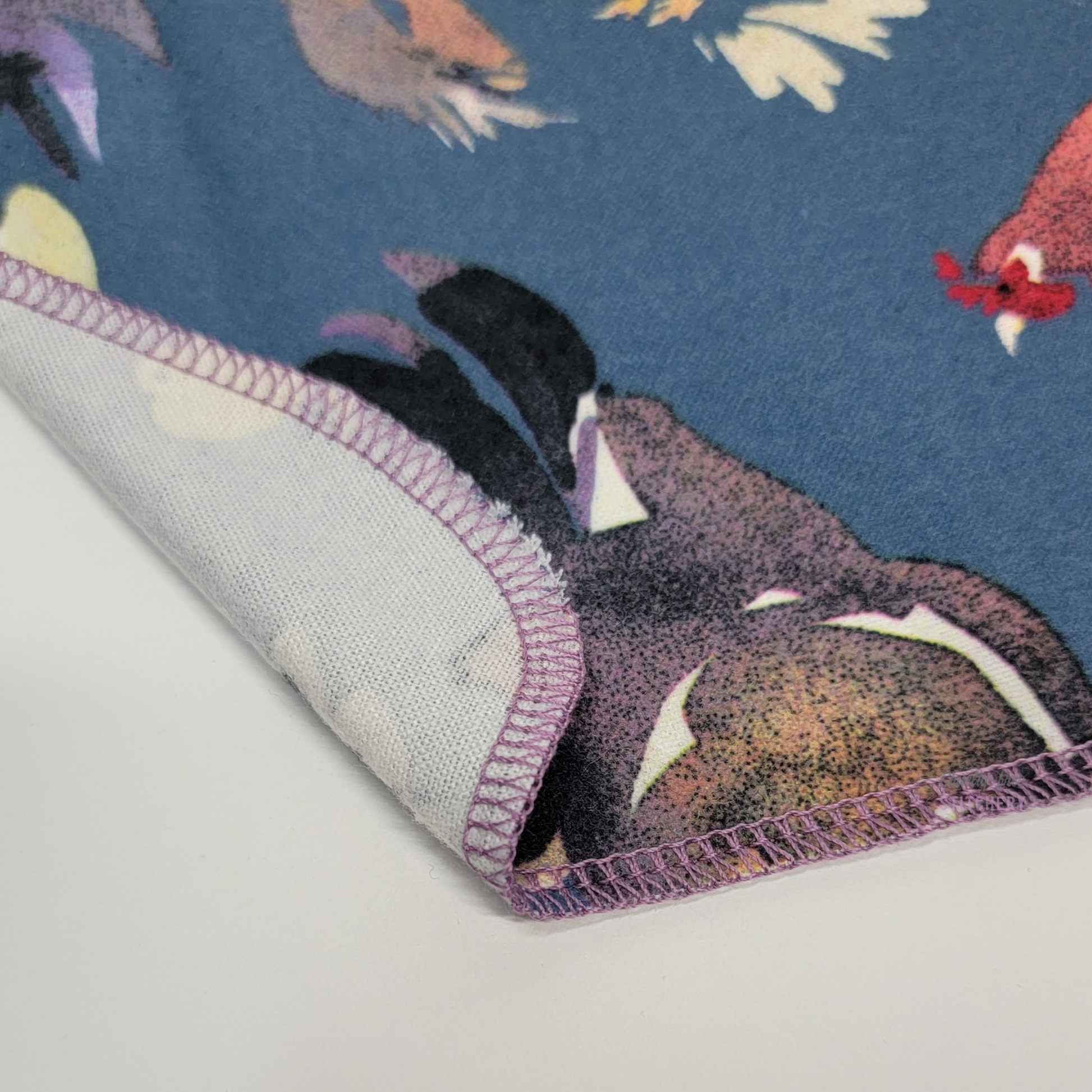 The blue chickens NonPaper towels close-up with the corner folded back to show that they are one layer of material and that the back is unprinted white. One of the chickens is peeking into the frame.