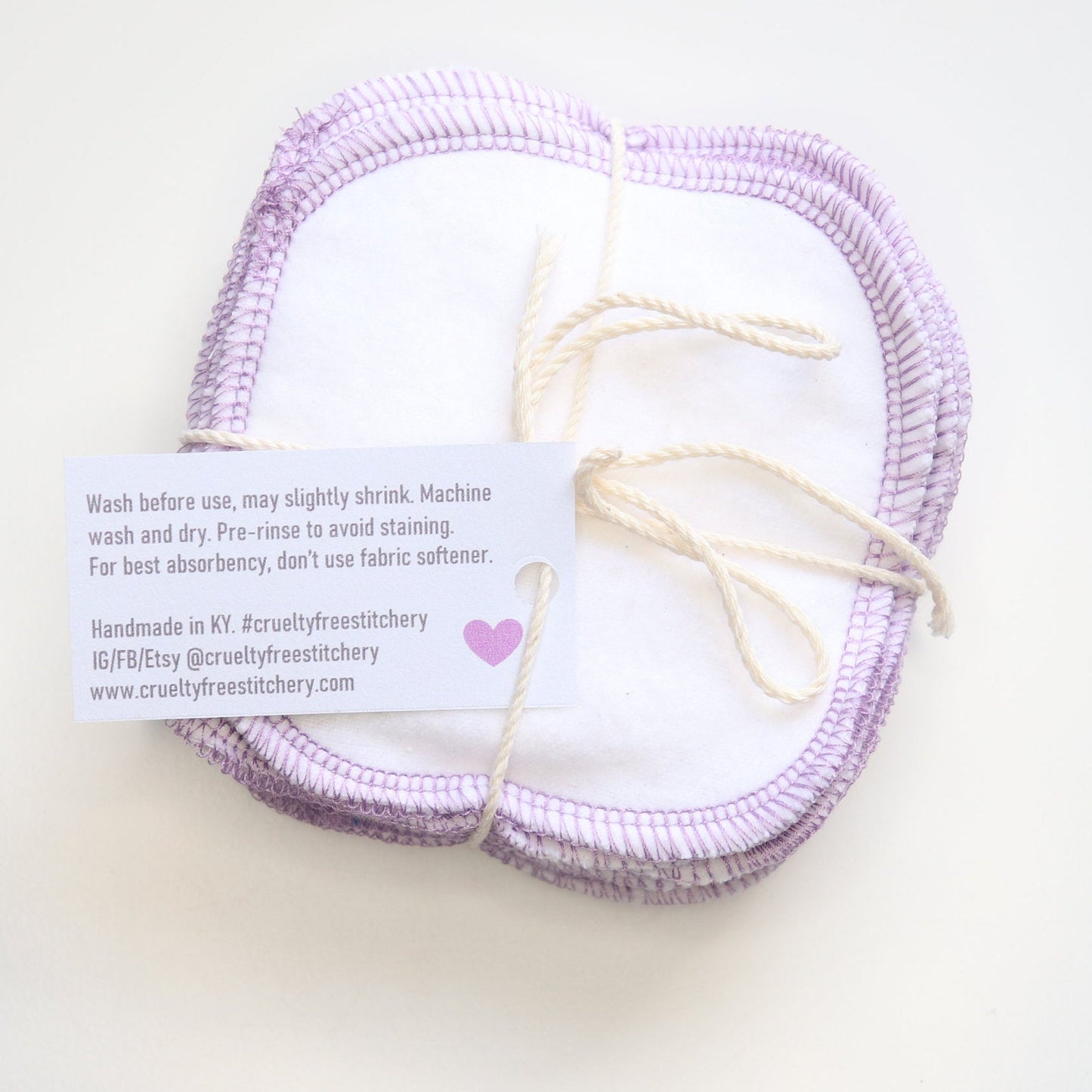 Bundle of white reusable cotton rounds with the back of the small paper tag showing with care instructions.