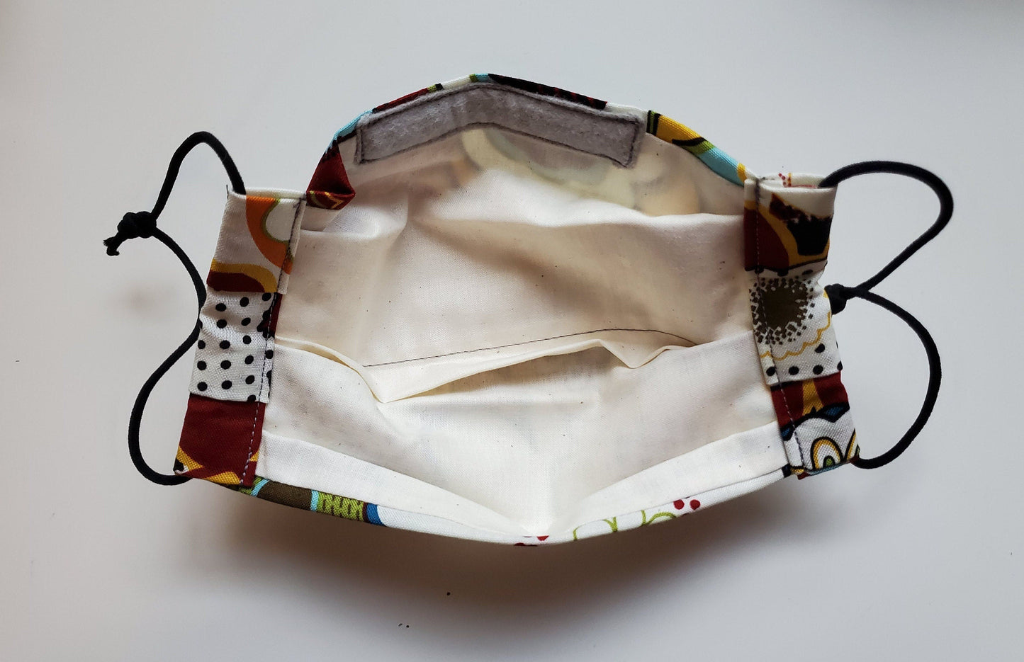 The back side of the mask, showing the natural cotton lining with a filter pocket, and a flannel encased nose wire at the top.