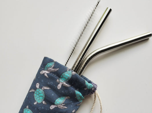 Reusable straw pouch with stainless steel straws sticking out the top. The fabric of the pouch is dark navy blue with tiny sea turtles printed all over, and it has a drawstring closure.