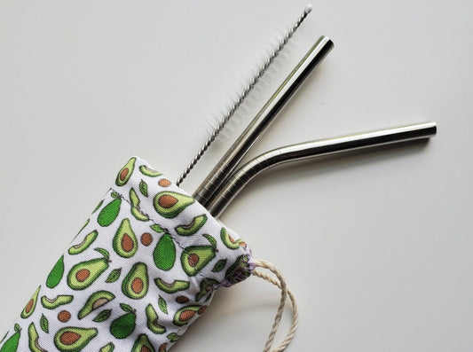 Reusable straw pouch with stainless steel straws sticking out the top. The fabric of the pouch is white with tiny avocados, some whole, some half, and some pits, and it has a drawstring closure.
