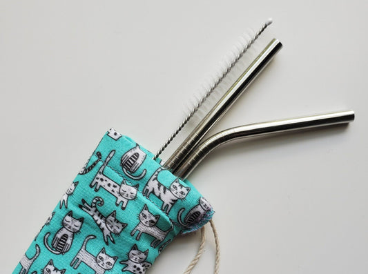 Reusable straw pouch with stainless steel straws sticking out the top. The fabric of the pouch is light blue with tiny black and white cats, and it has a drawstring closure.