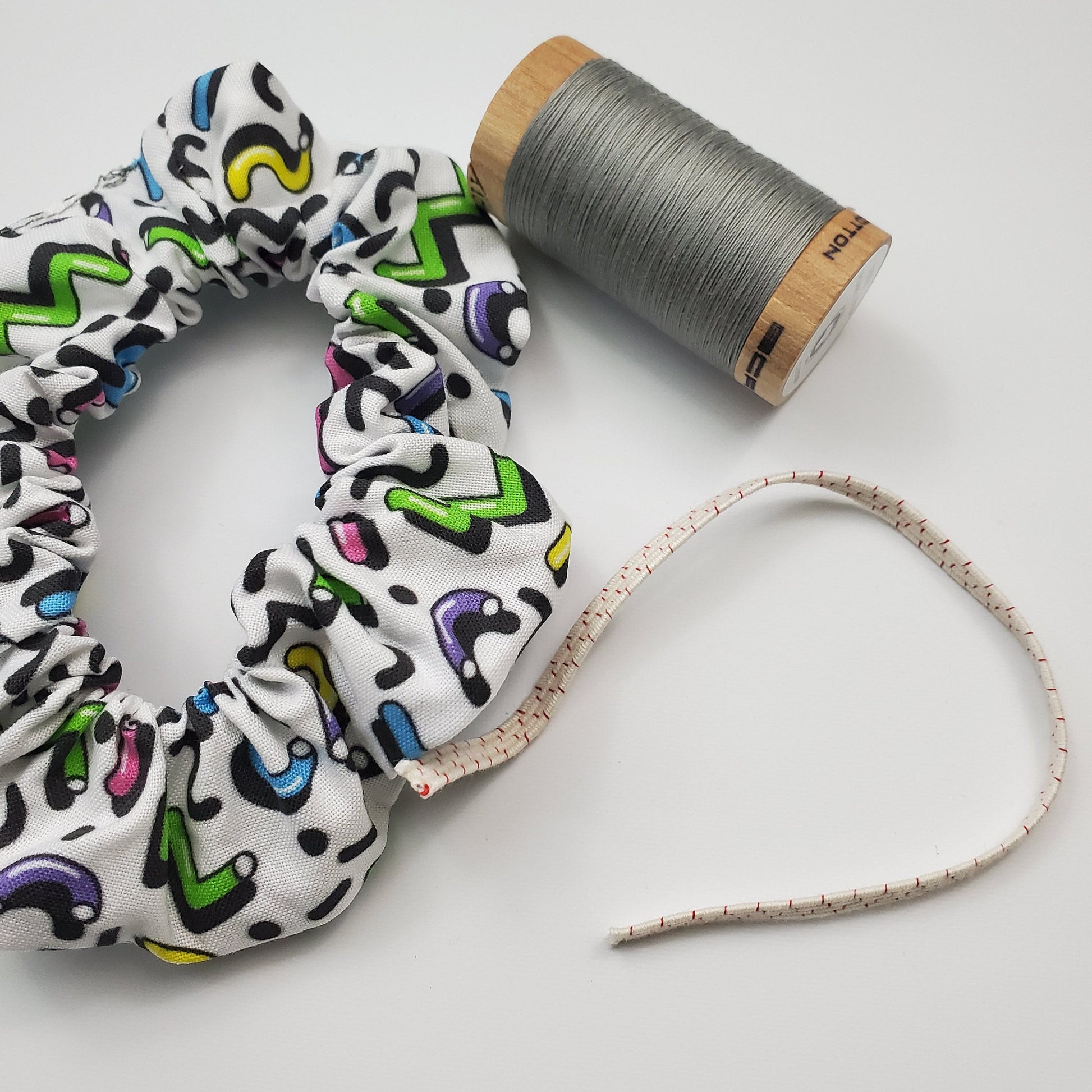 Scrunchie shown next to a wooden spool of grey thread, and a piece of the biodegradable elastic.