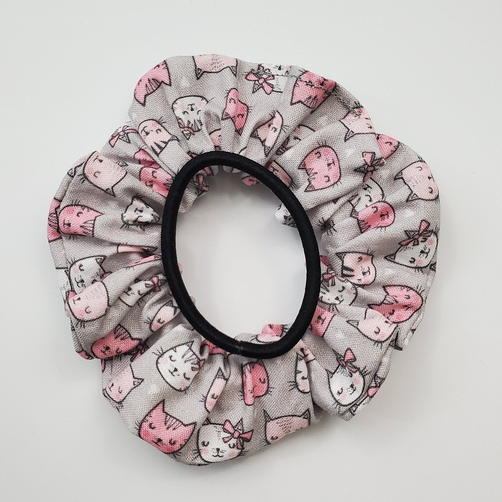Grey and pink cats scrunchie shown with a black hair tie as a size comparison.