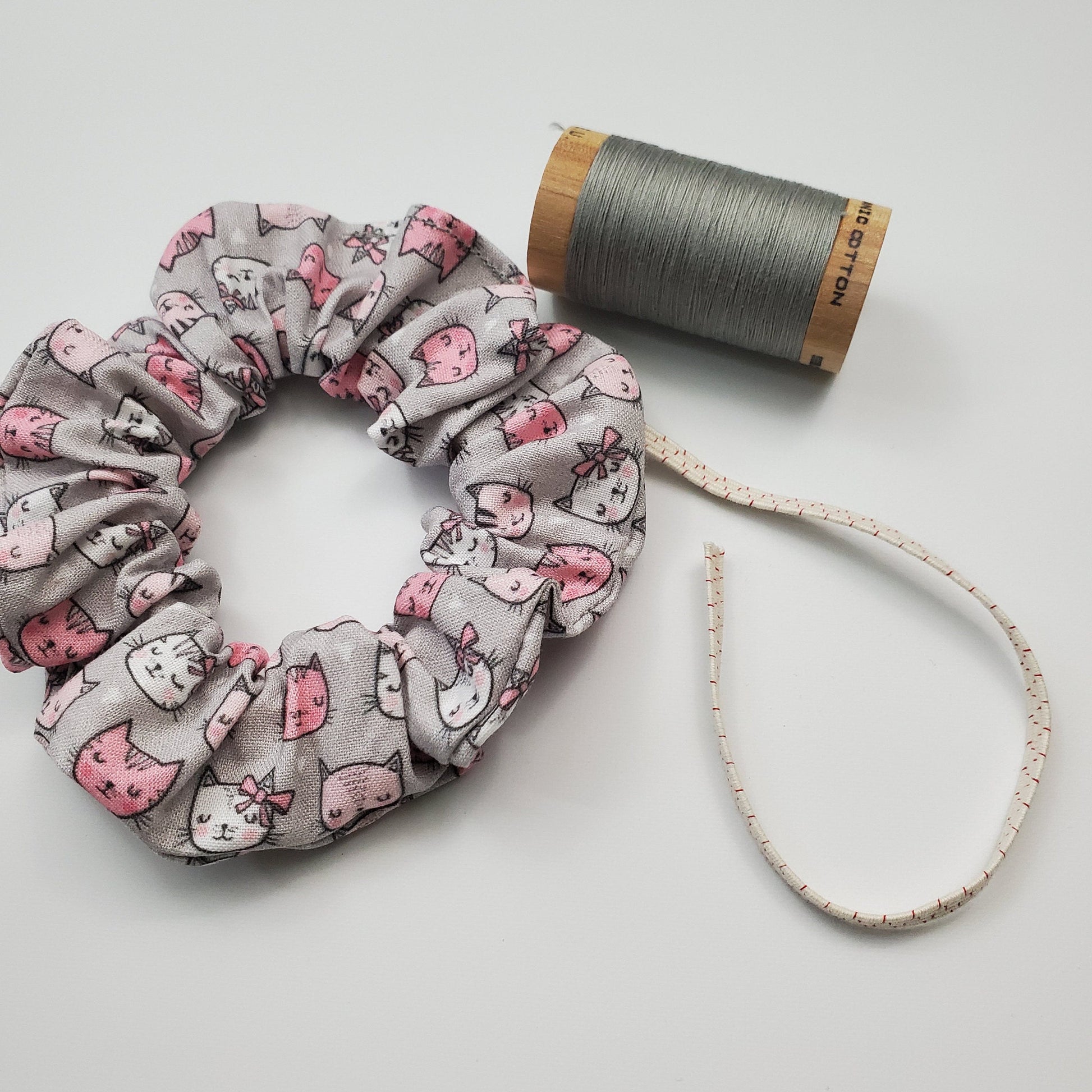 Scrunchie next to a wooden spool of gray thread and a piece of the biodegradable elastic.