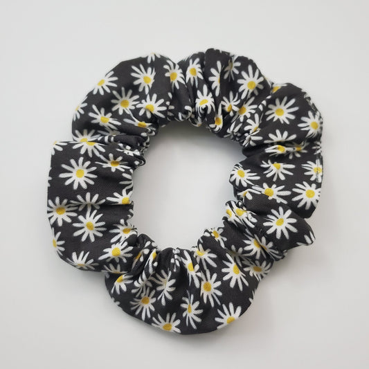 Black scrunchie with tiny white daisies. They daisies are simple with a tiny yellow dot in the center.