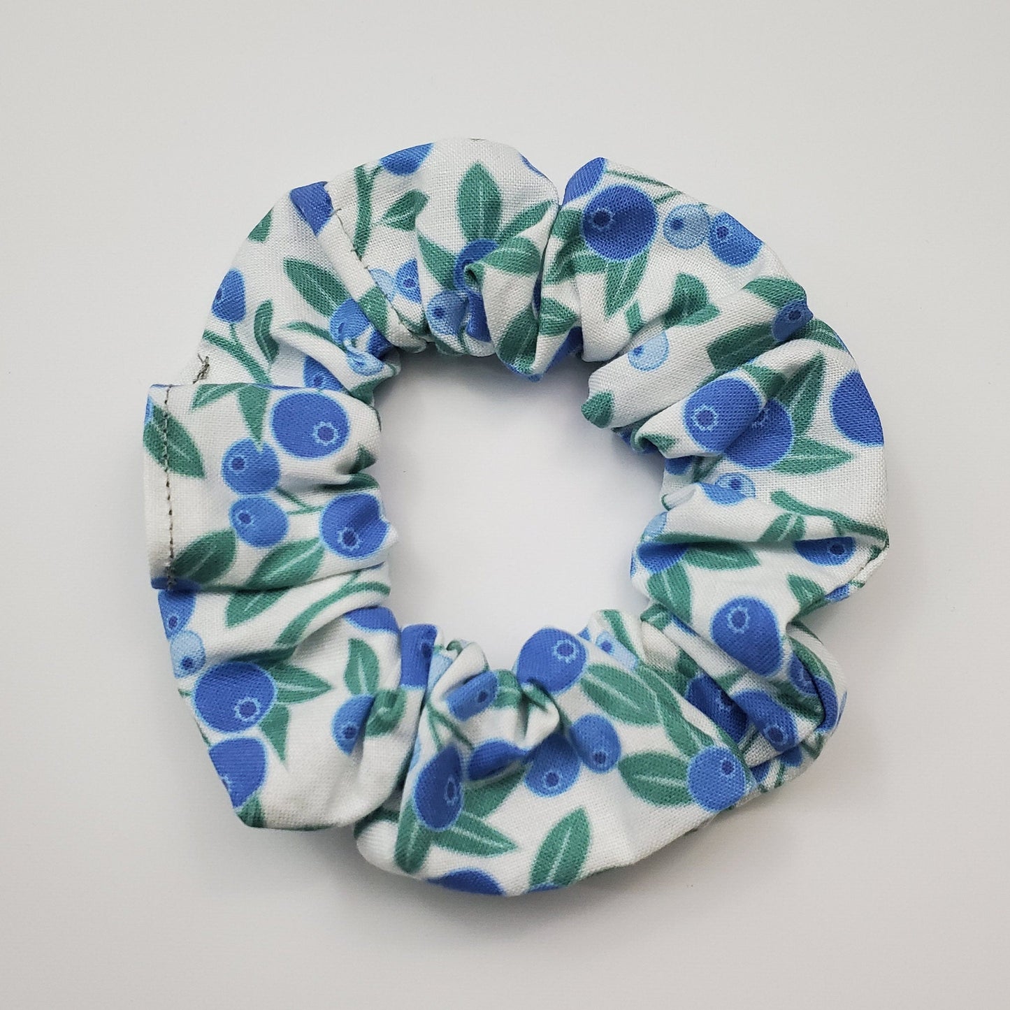 Blueberry print scrunchie - a white background fabric with solid color dark and light blue blueberries and green leaves.